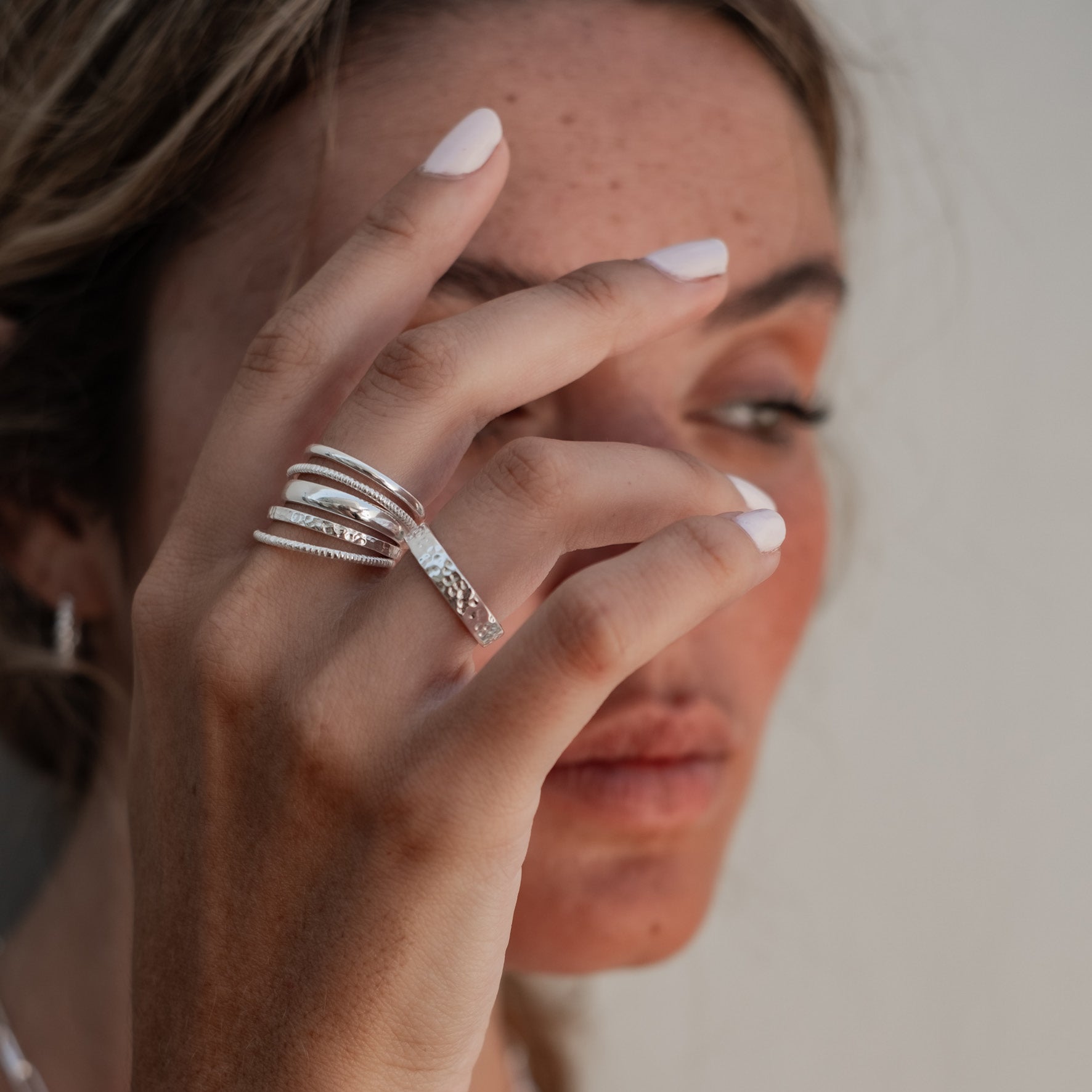 A woman covering her eyes with one hand, wearing multiple silver rings and white nail polish.
