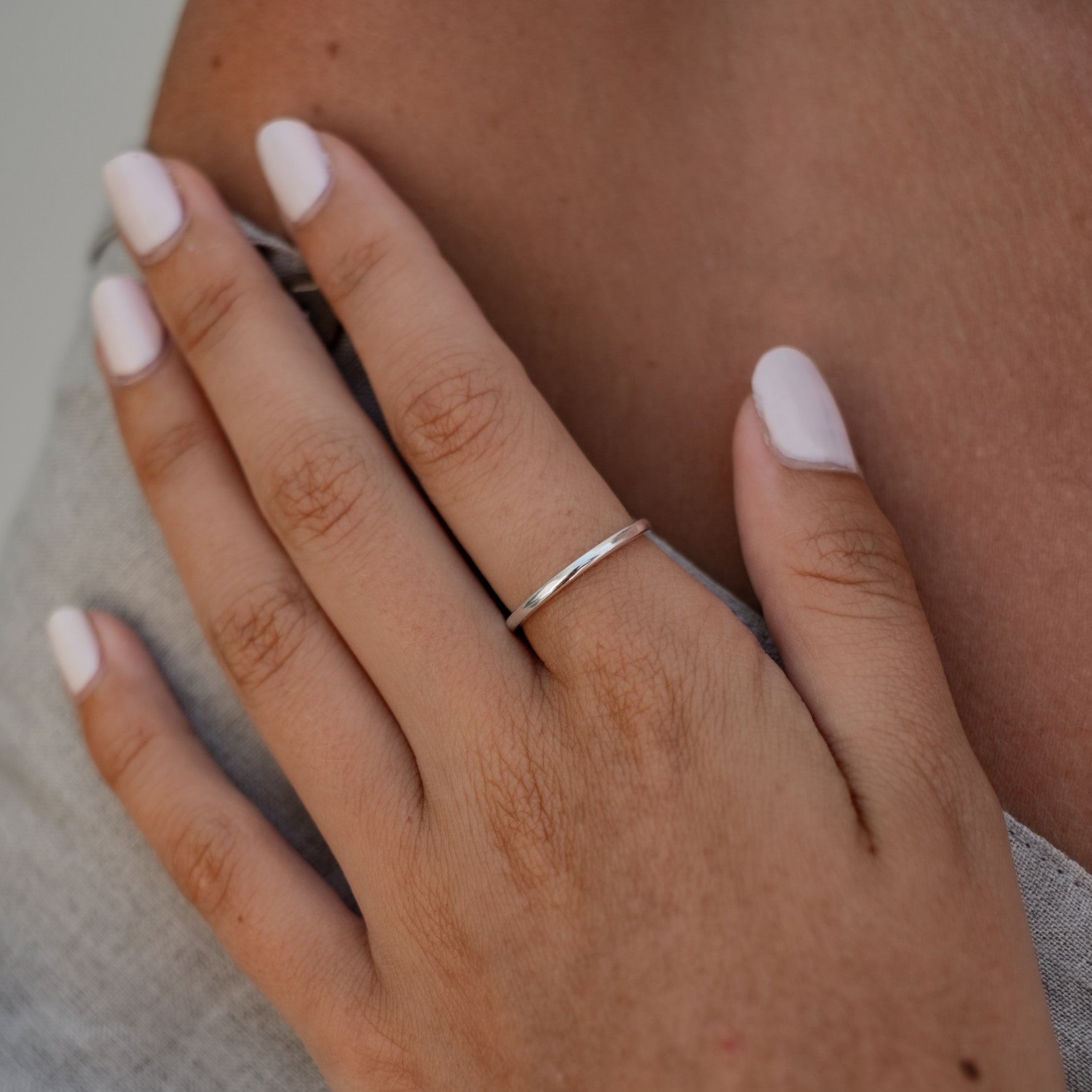 A person wearing a slim silver ring on their finger, with their hand resting on their arm.