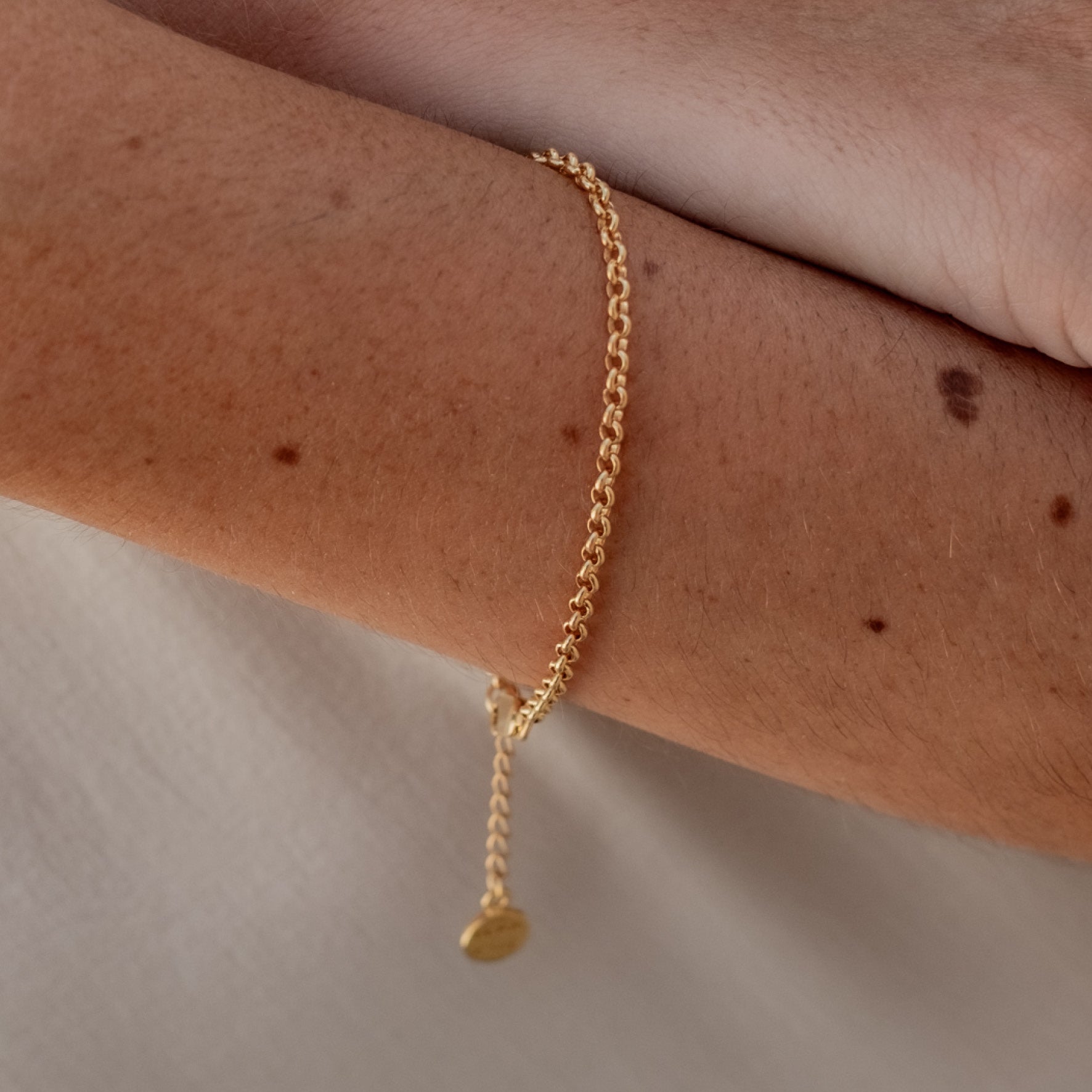 Close-up of a woman's wrist wearing a gold chain bracelet with an adjustable clasp and circular charm.