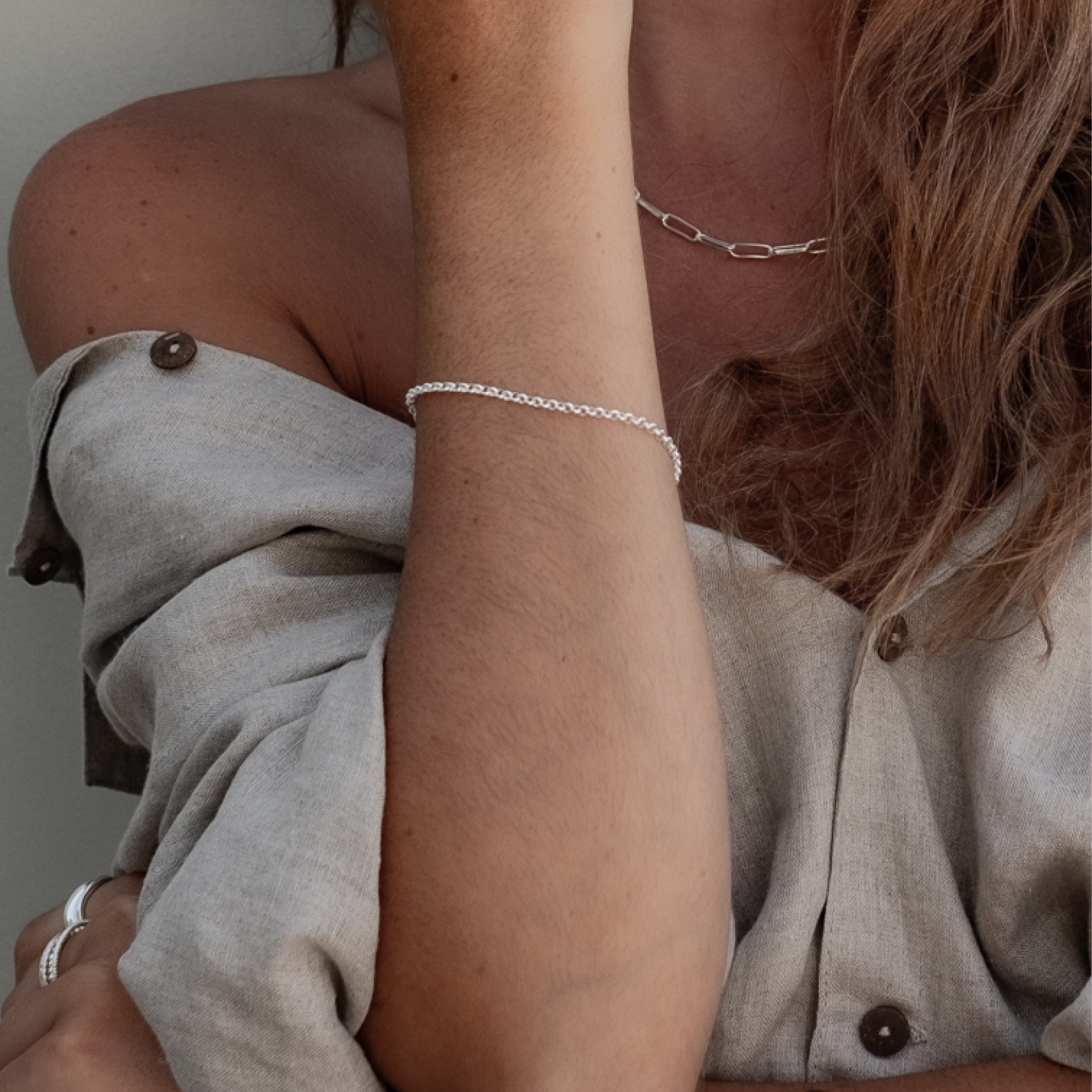 Close-up of a woman's wrist wearing a silver chain bracelet with an adjustable clasp and circular charm.