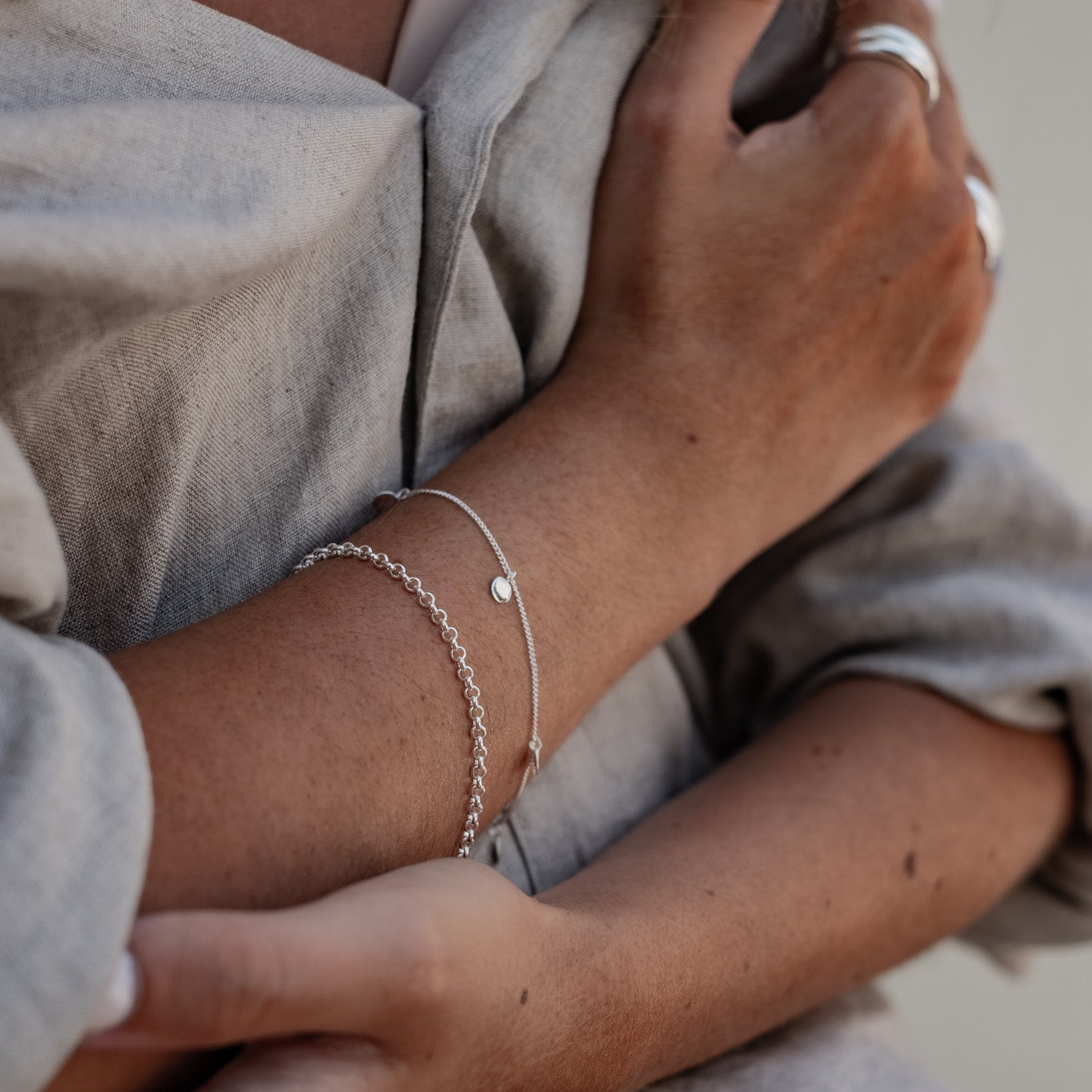 Close-up of a woman's wrist wearing a silver chain bracelet and and one with charms