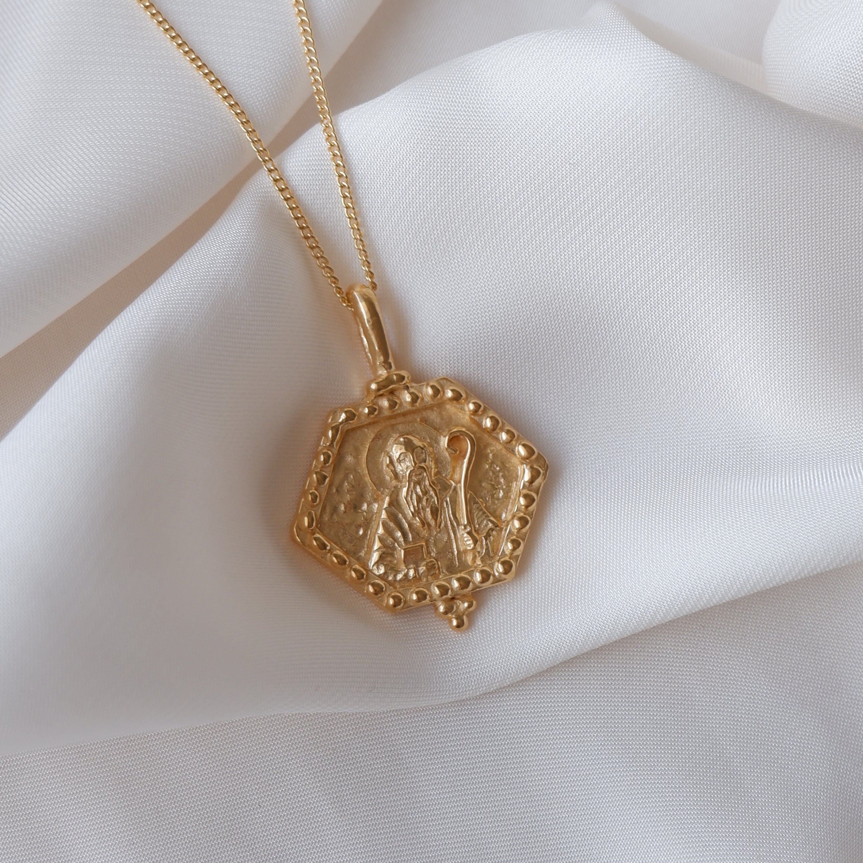 St Benedict necklace gold flat lay in white fabric
