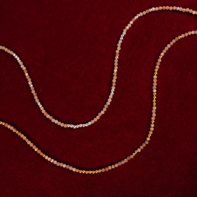 close-up of two gemstone pink blush necklaces resting on red fabric