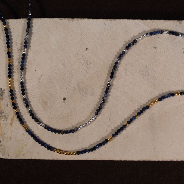 close-up of two blue gemstone necklaces resting on a creme textured background