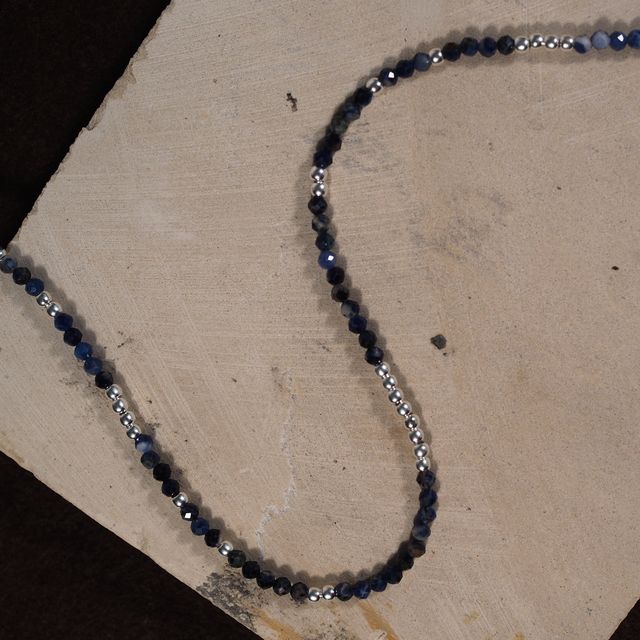 blue gemstone necklace with silver beads laid on a pink textured background