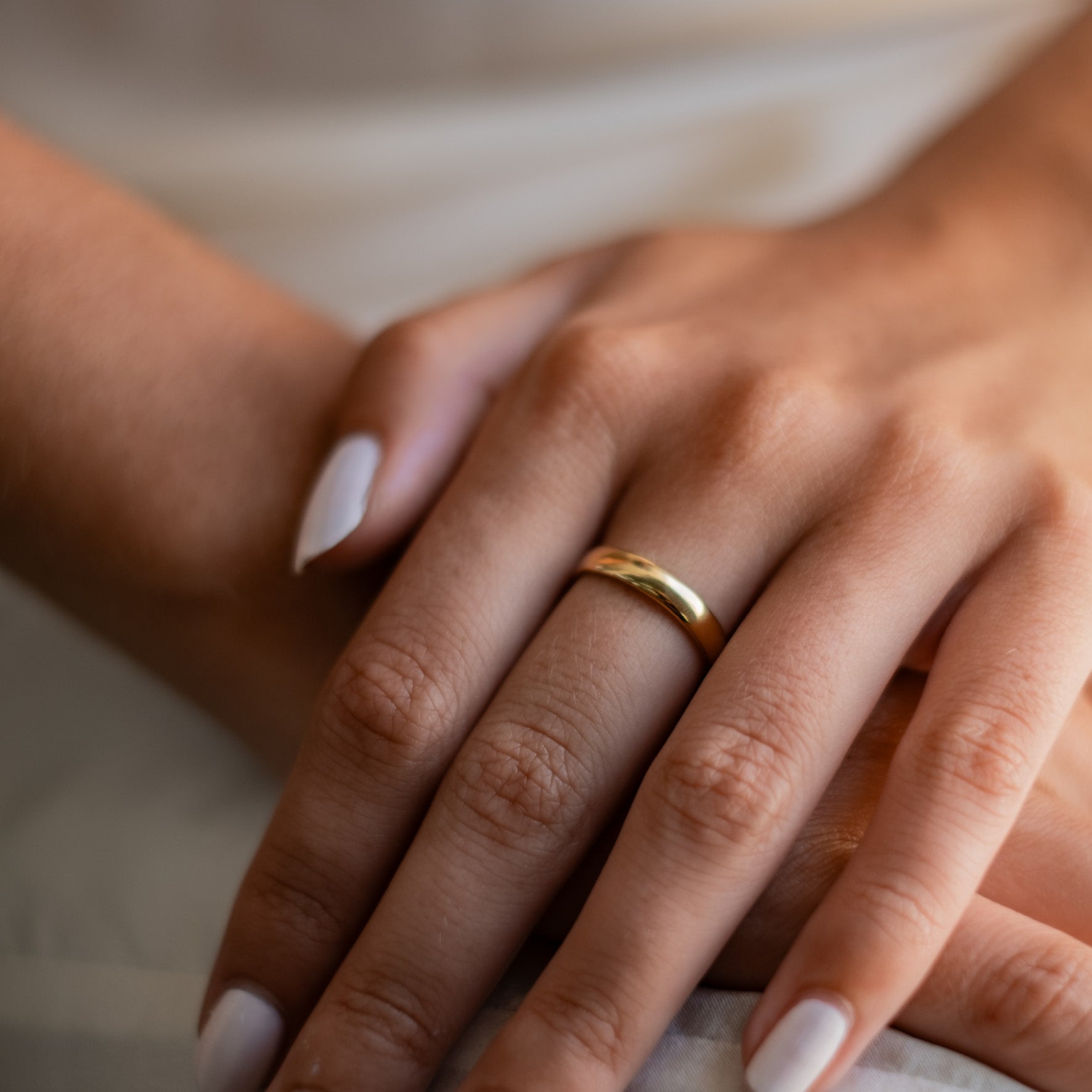 A person featuring a gold ring on their finger, with their hands gently clasped together.