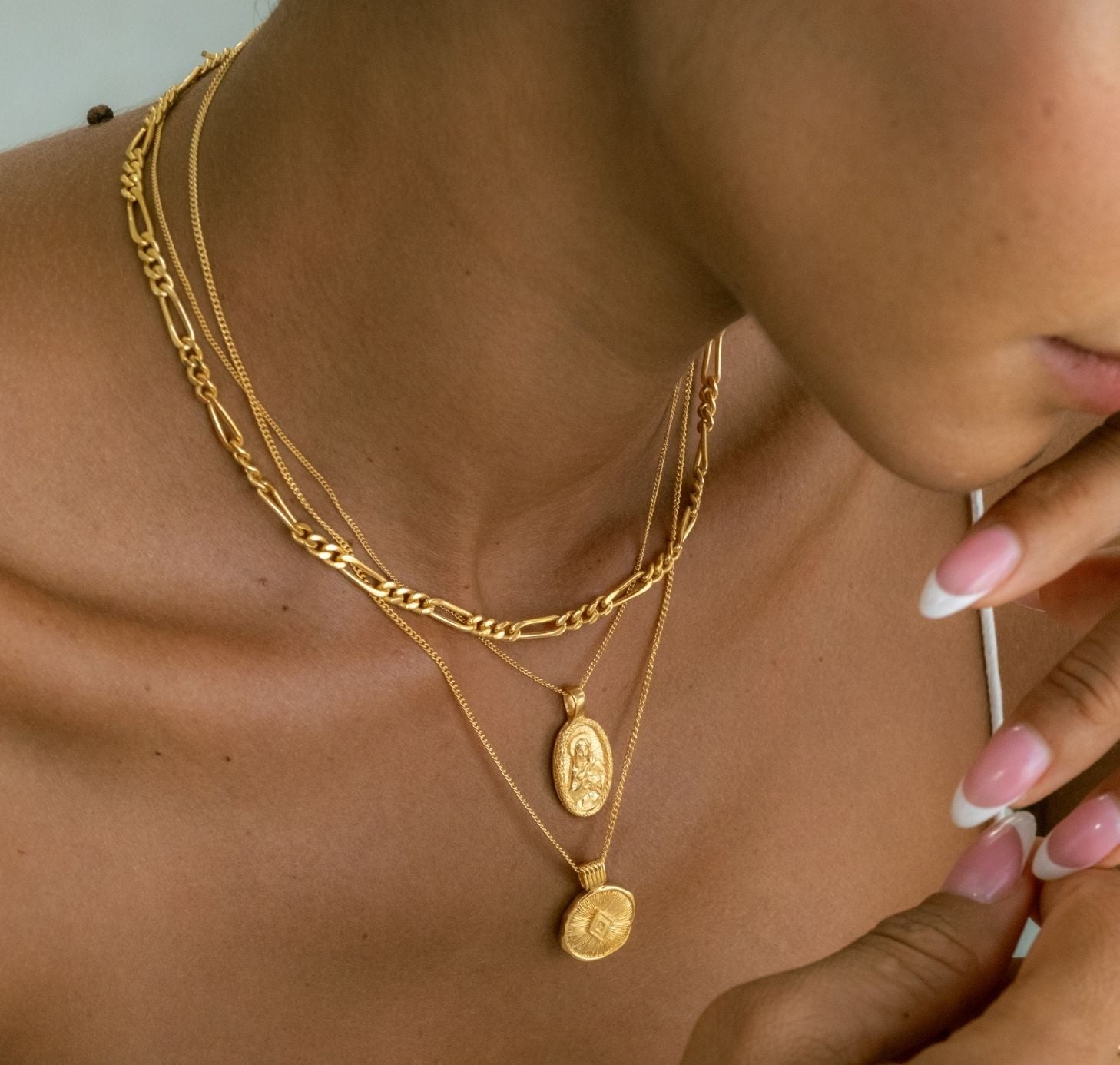 a woman wearing three layers necklaces gold