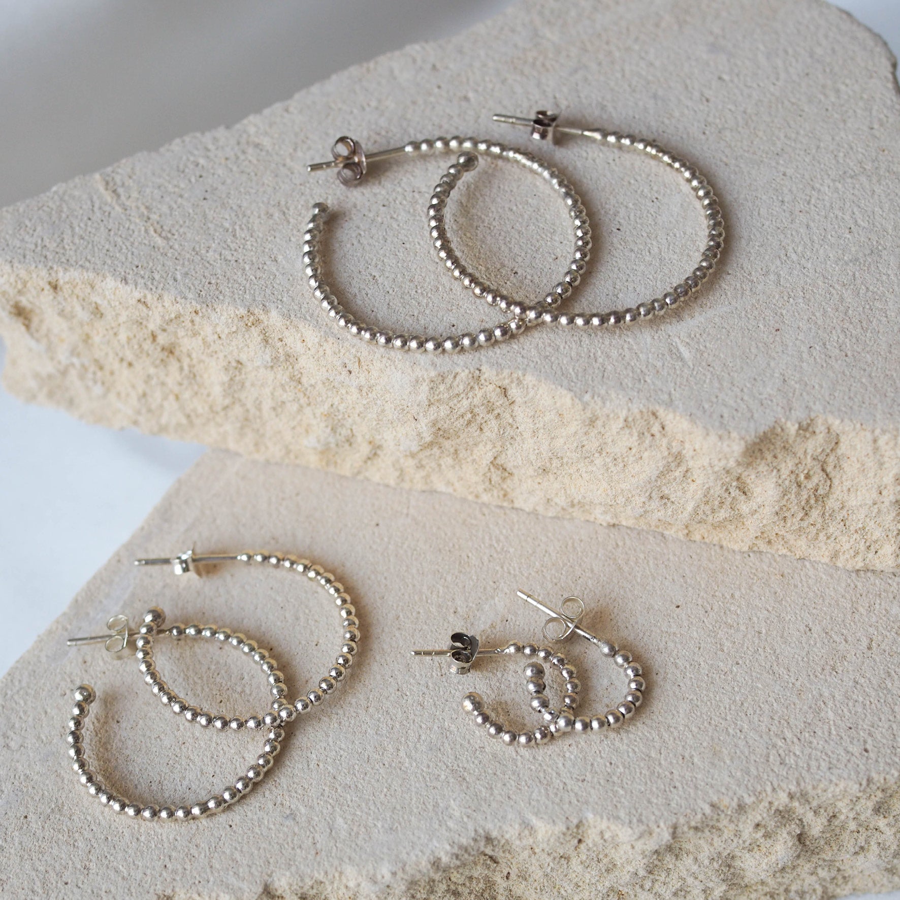 Multiple silver earrings displayed on a textured beige stone