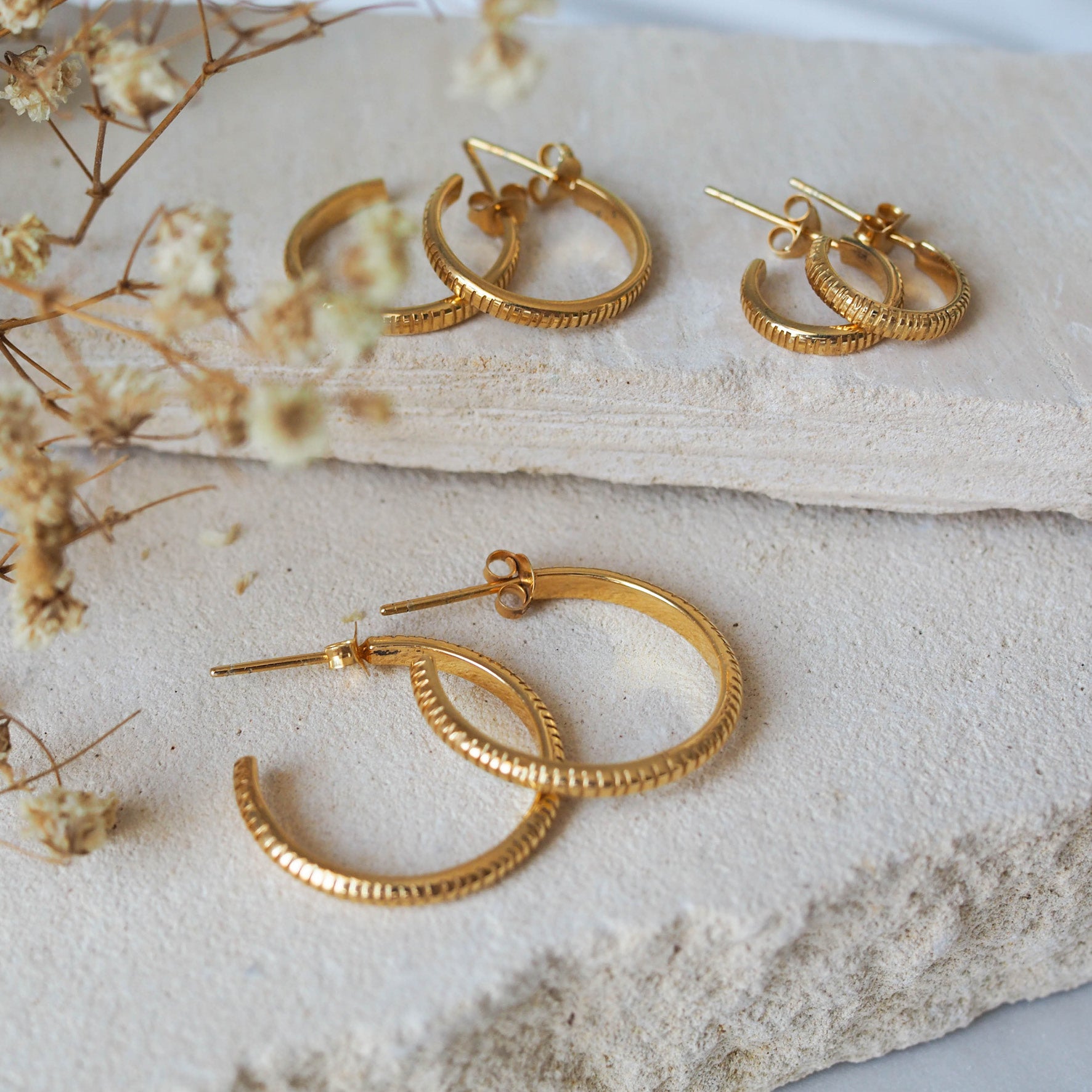 The MET Stripe Thin Earrings in three pairs sizes displayed on beige stone