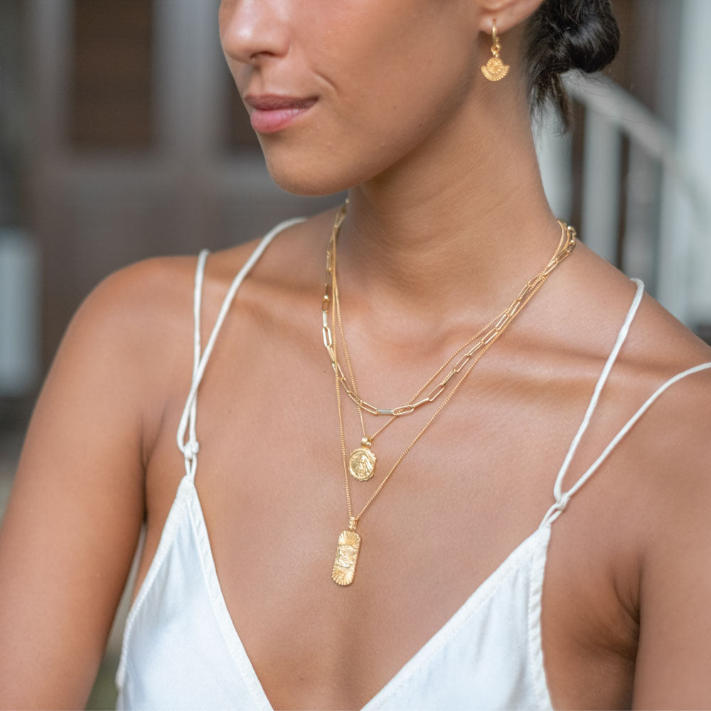 a woman with white dress wearing multiple necklaces gold and earrings gold