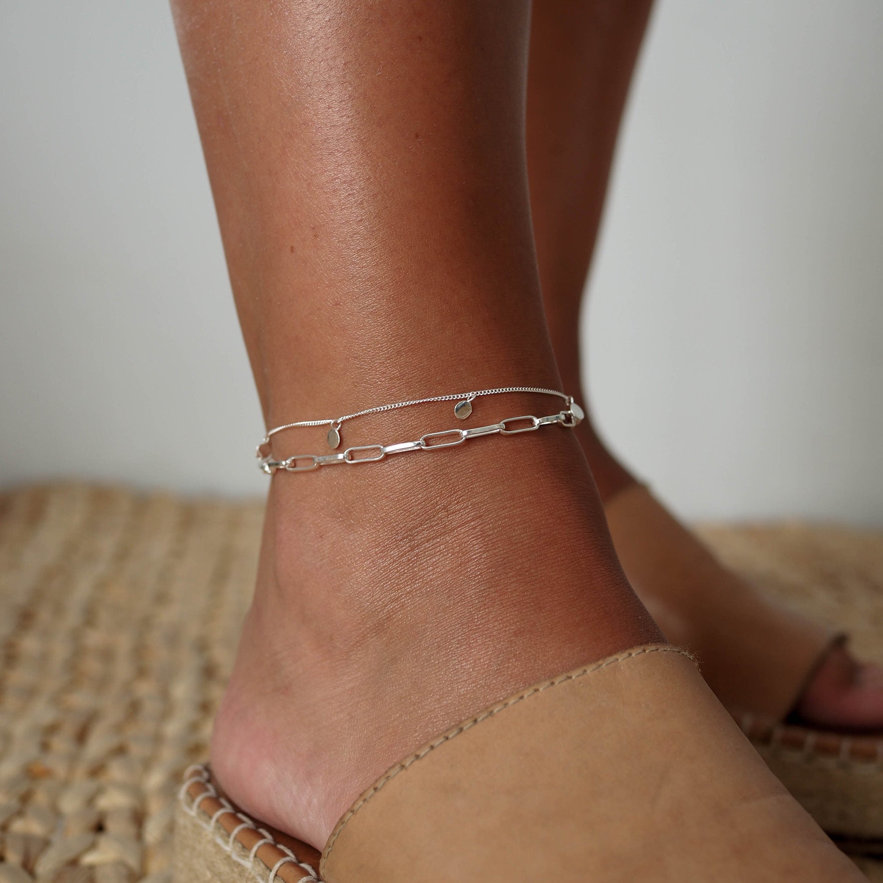 a woman with leather sandals wearing two anklets silver on her
