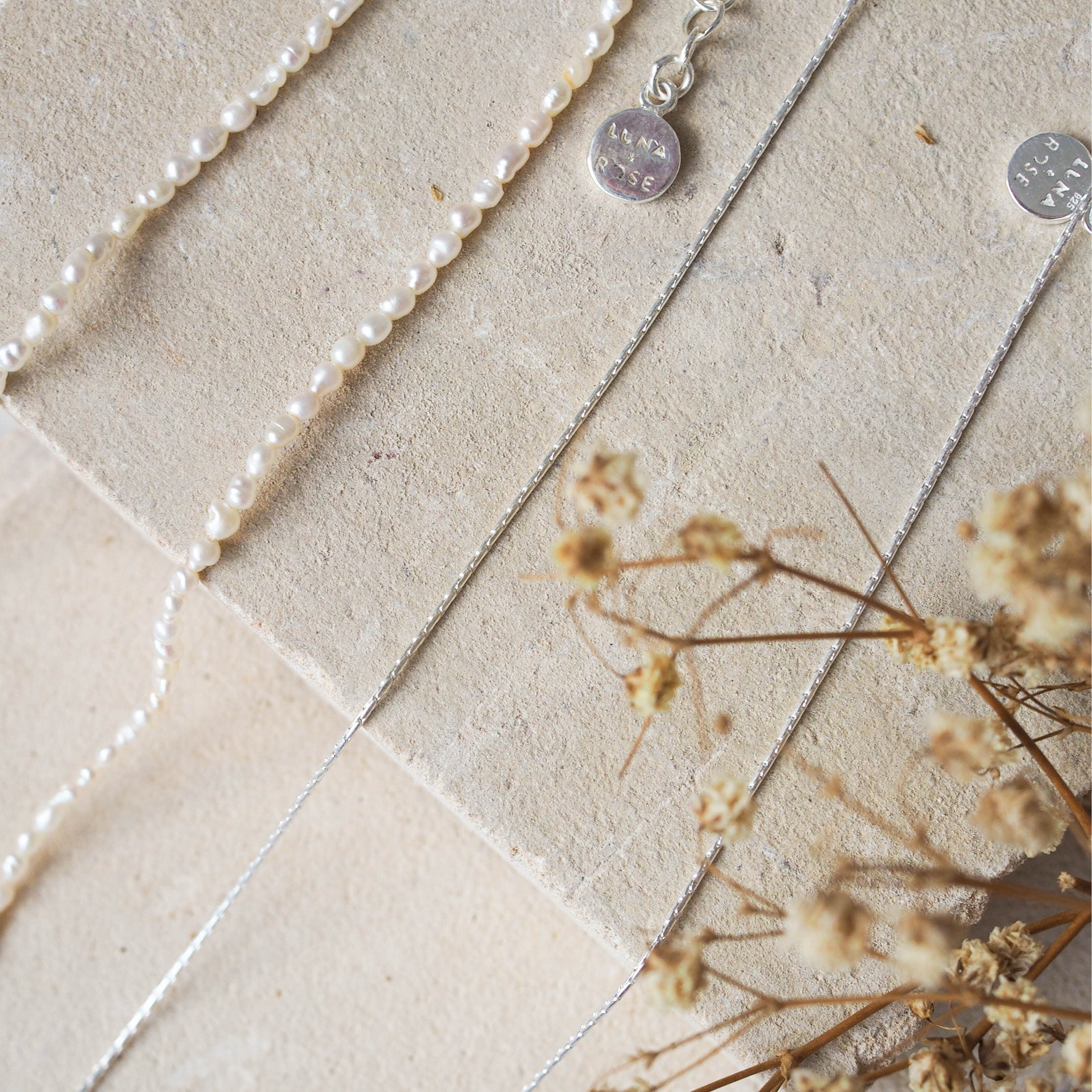 two silver necklaces displayed on beige stone