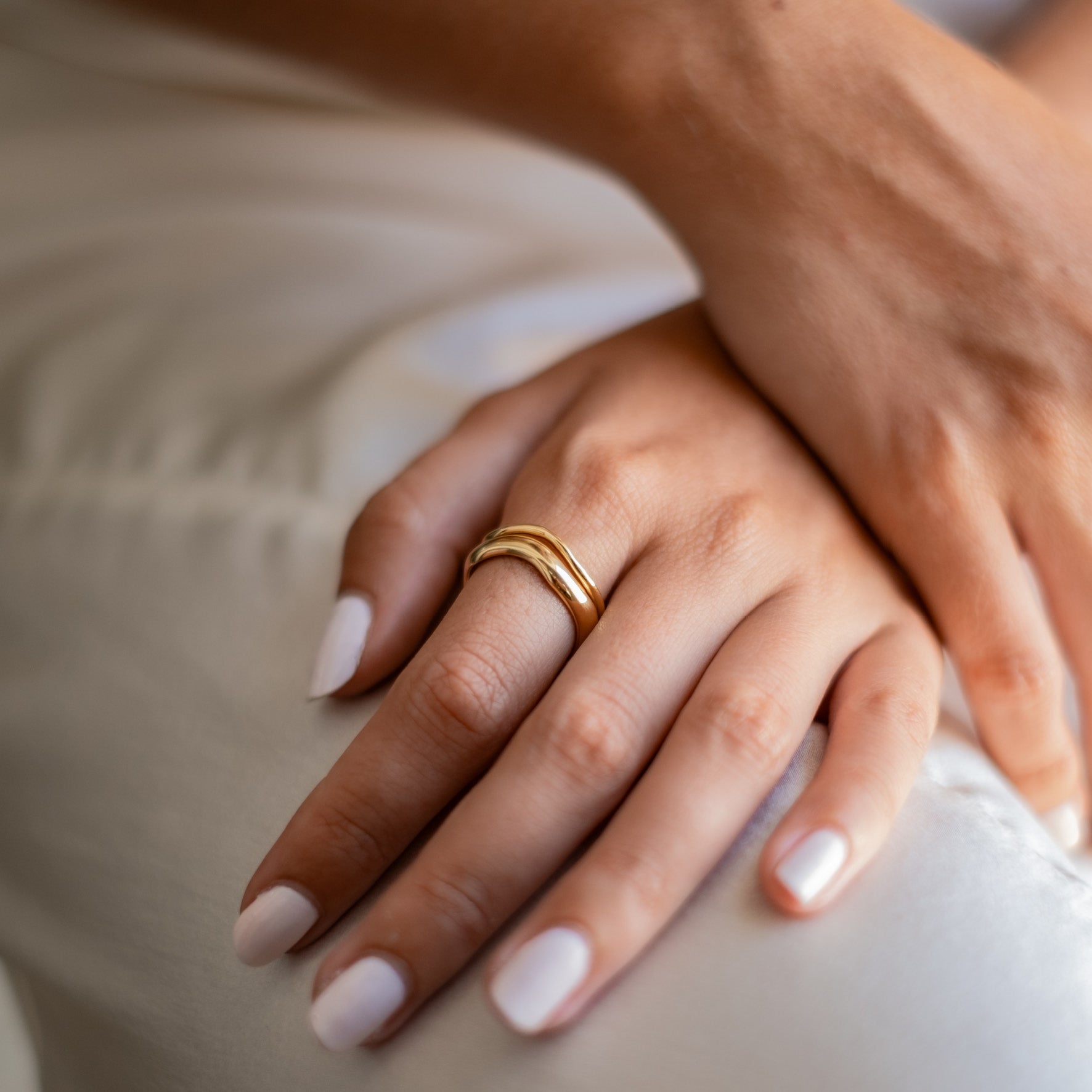Close-up of a woman's arms crossed over her chest, showcasing multiple gold rings with various designs on her fingers.