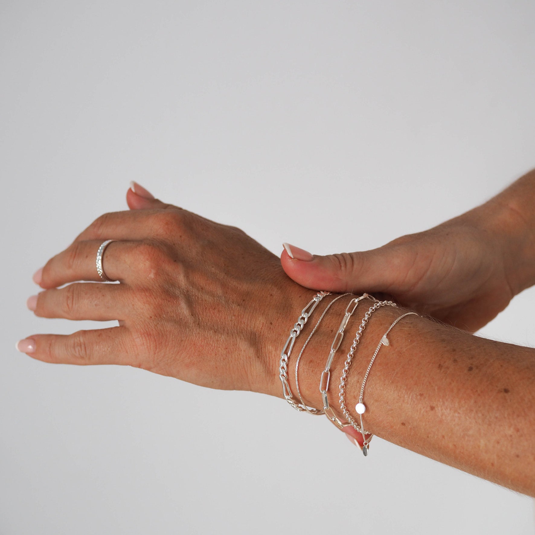 A person wearing multiple silver bracelets on their wrist, including link chains, combined with a silver ring.
