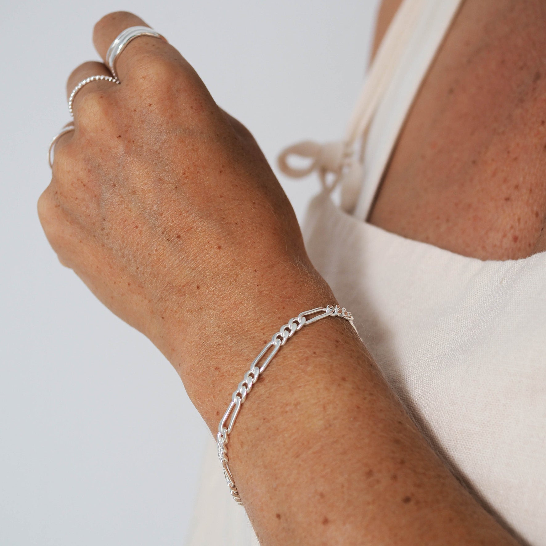 A person wearing a silver link chain bracelet and silver rings on their fingers.