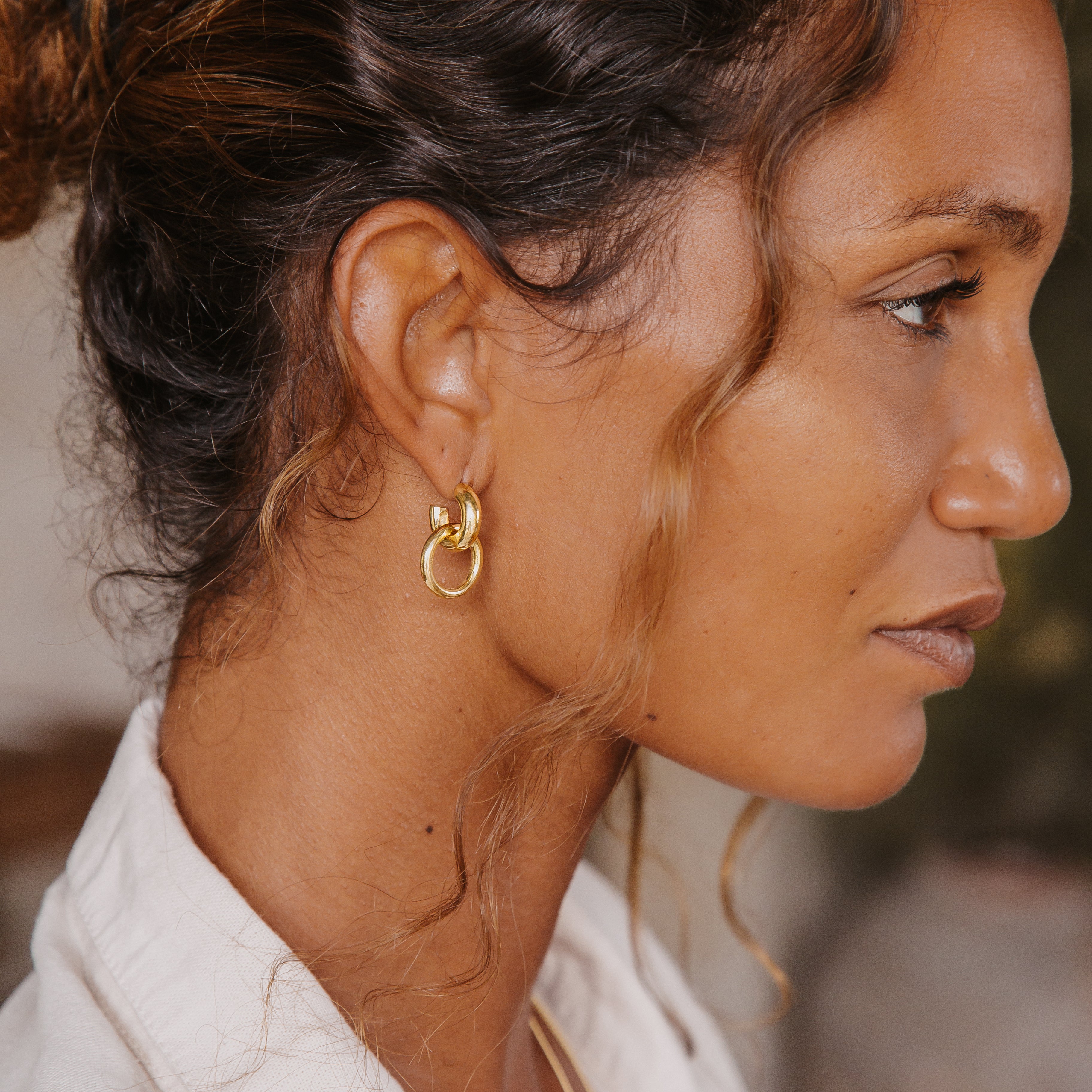 A close-up side view of a woman wearing the double hoop gold earrings, with her hair styled back to showcase the jewelry.
