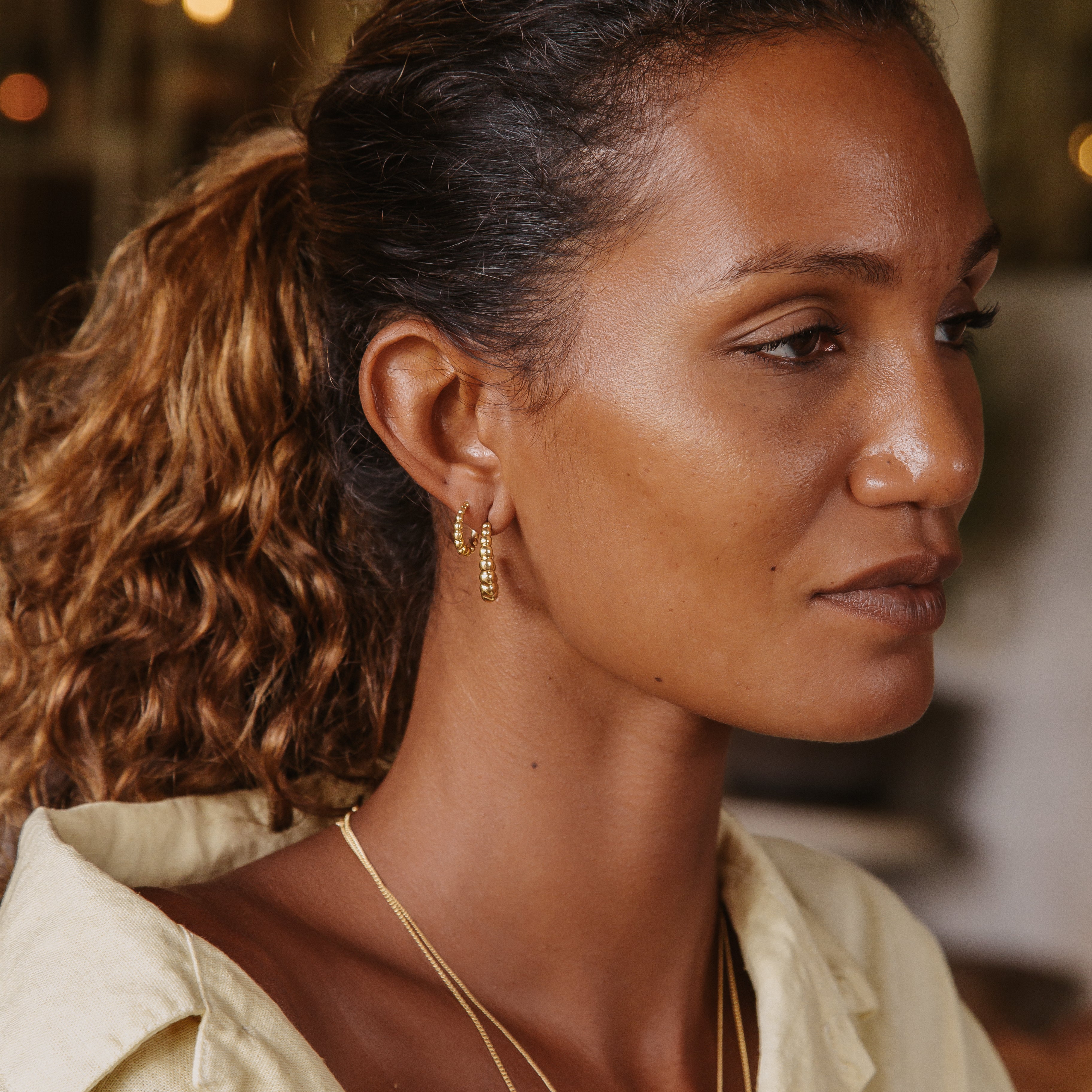 A woman with brown hair wearing two golden earrings and a yellow blouse