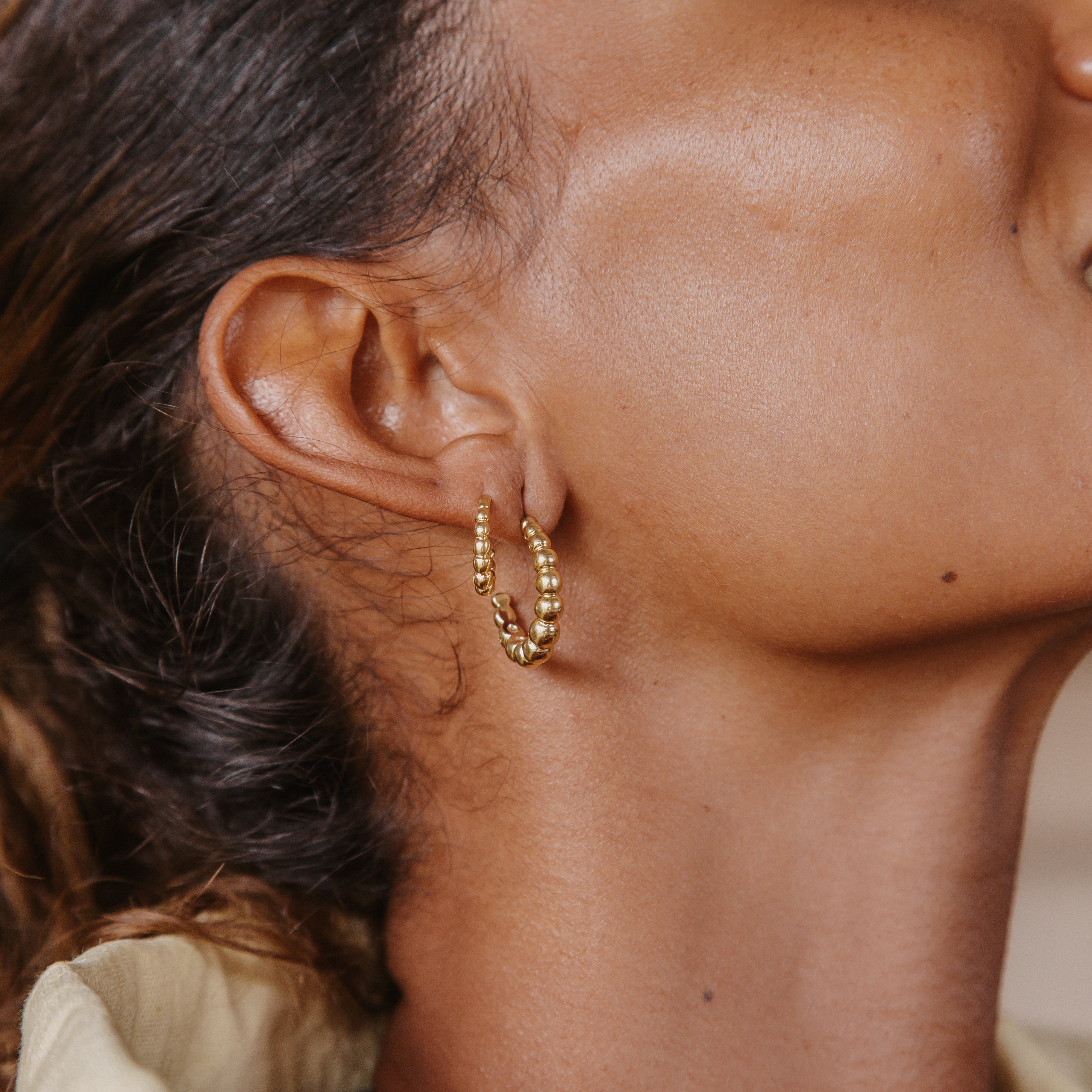 Close-up of a woman with brown hair wearing two small golden earrings