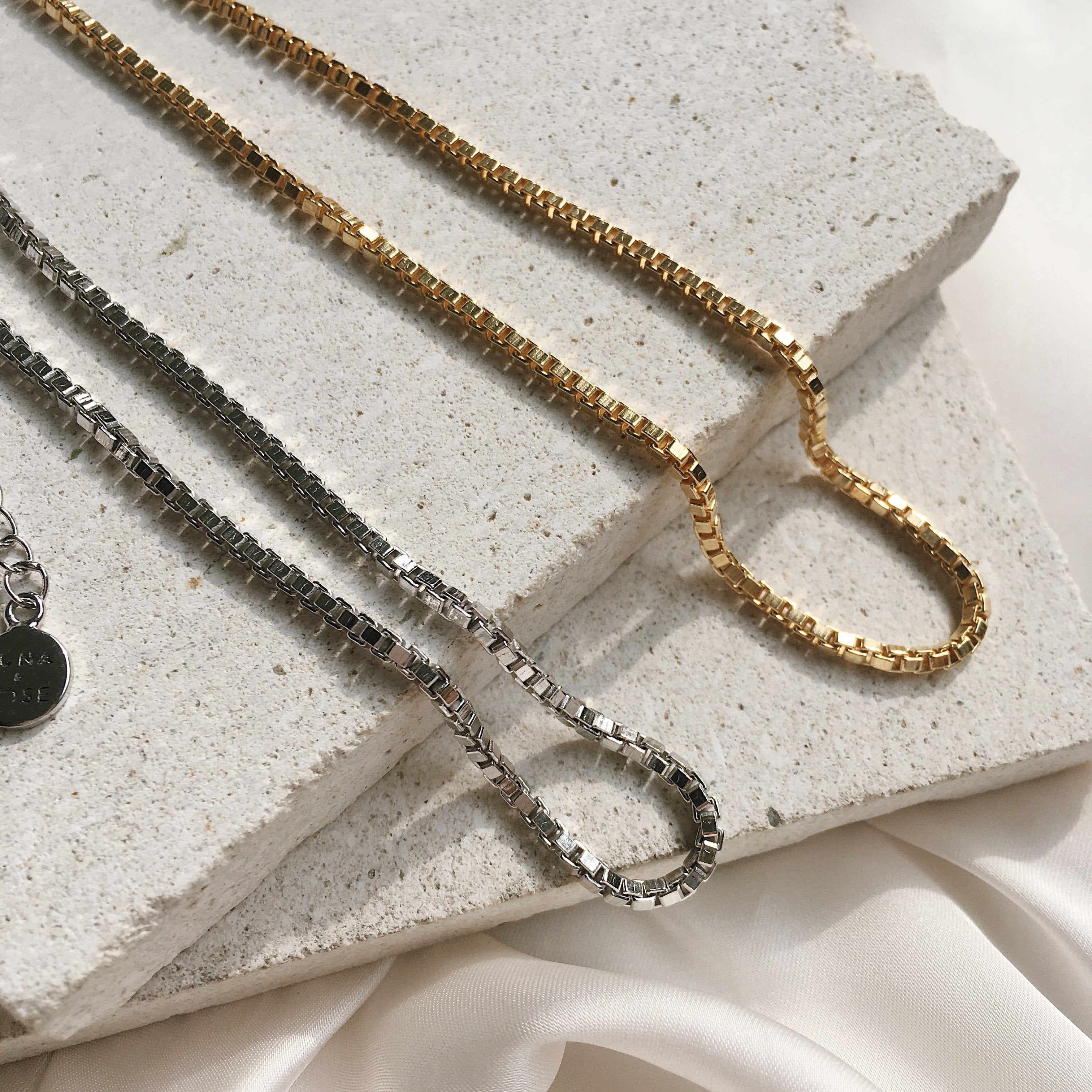Close-up of a golden and silver necklace displayed on a light stone surface