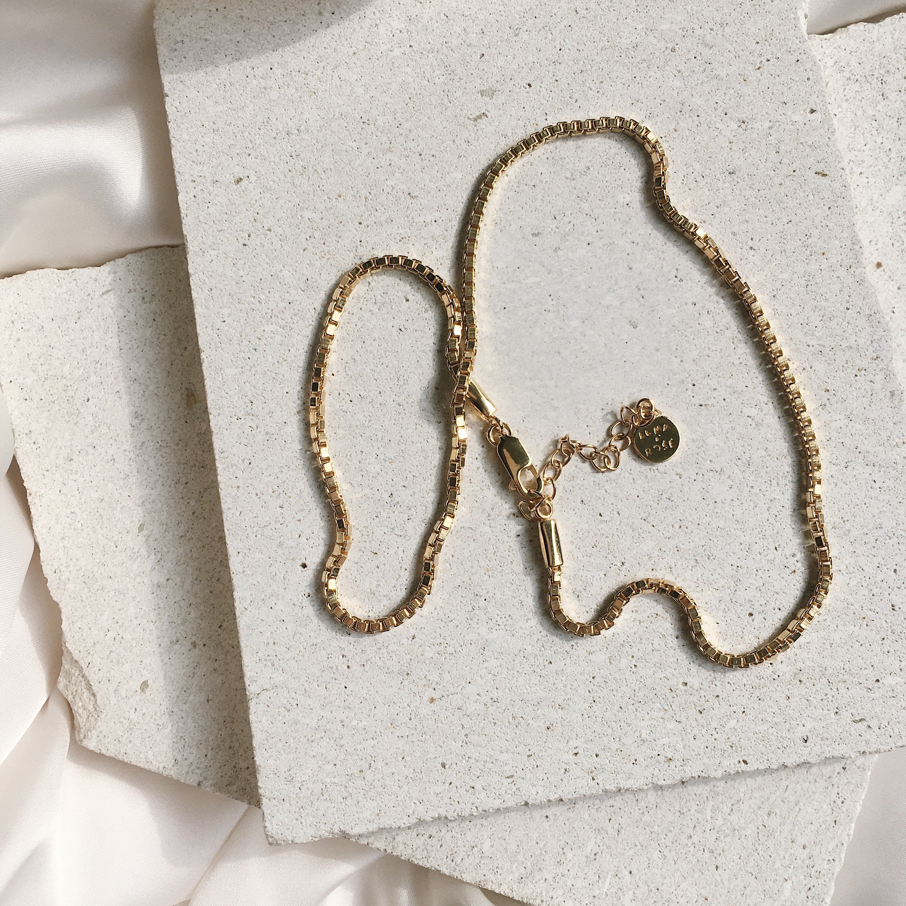 A golden necklace displayed on a light stone surface