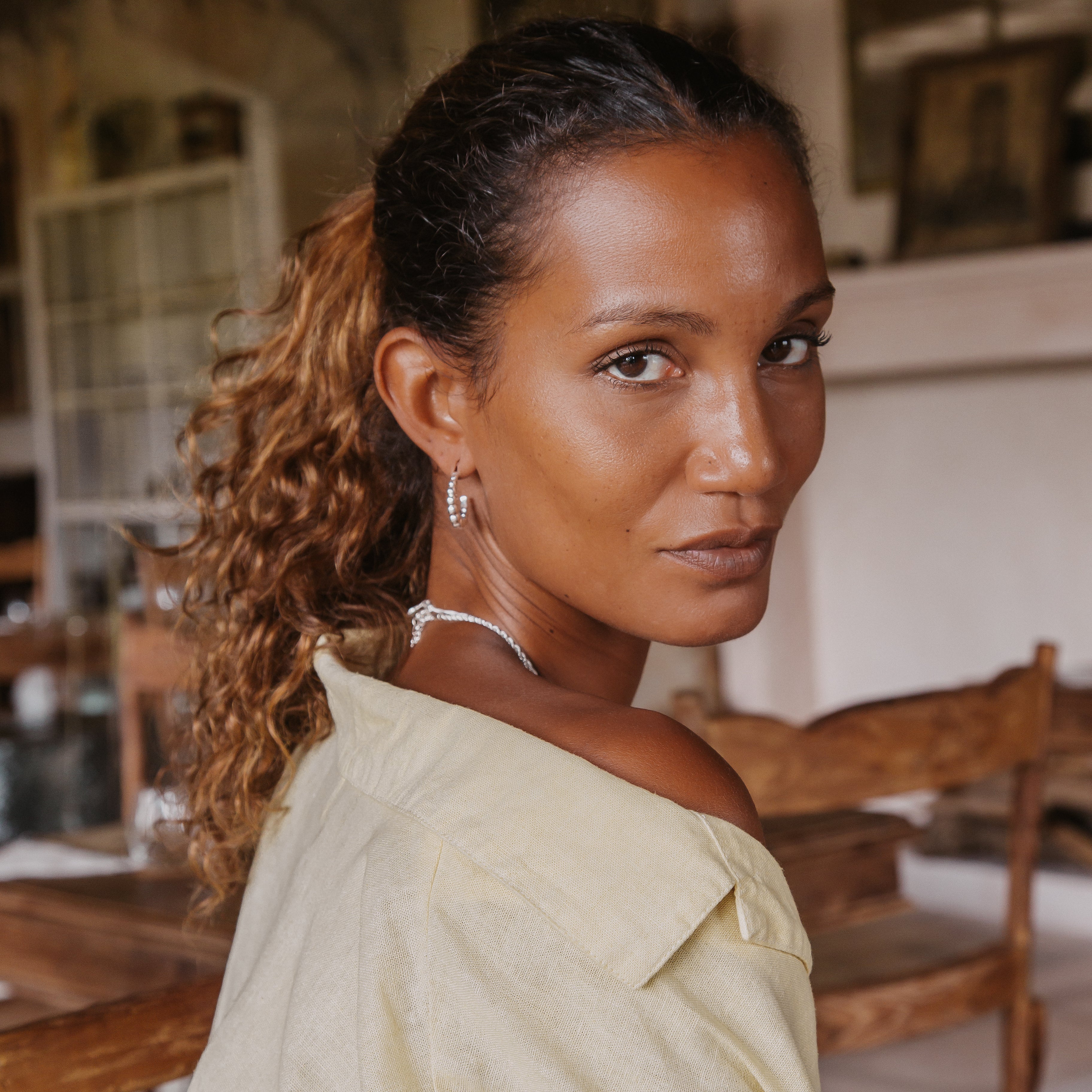 A woman with brown hair wearing a silver earring and a yellow blouse