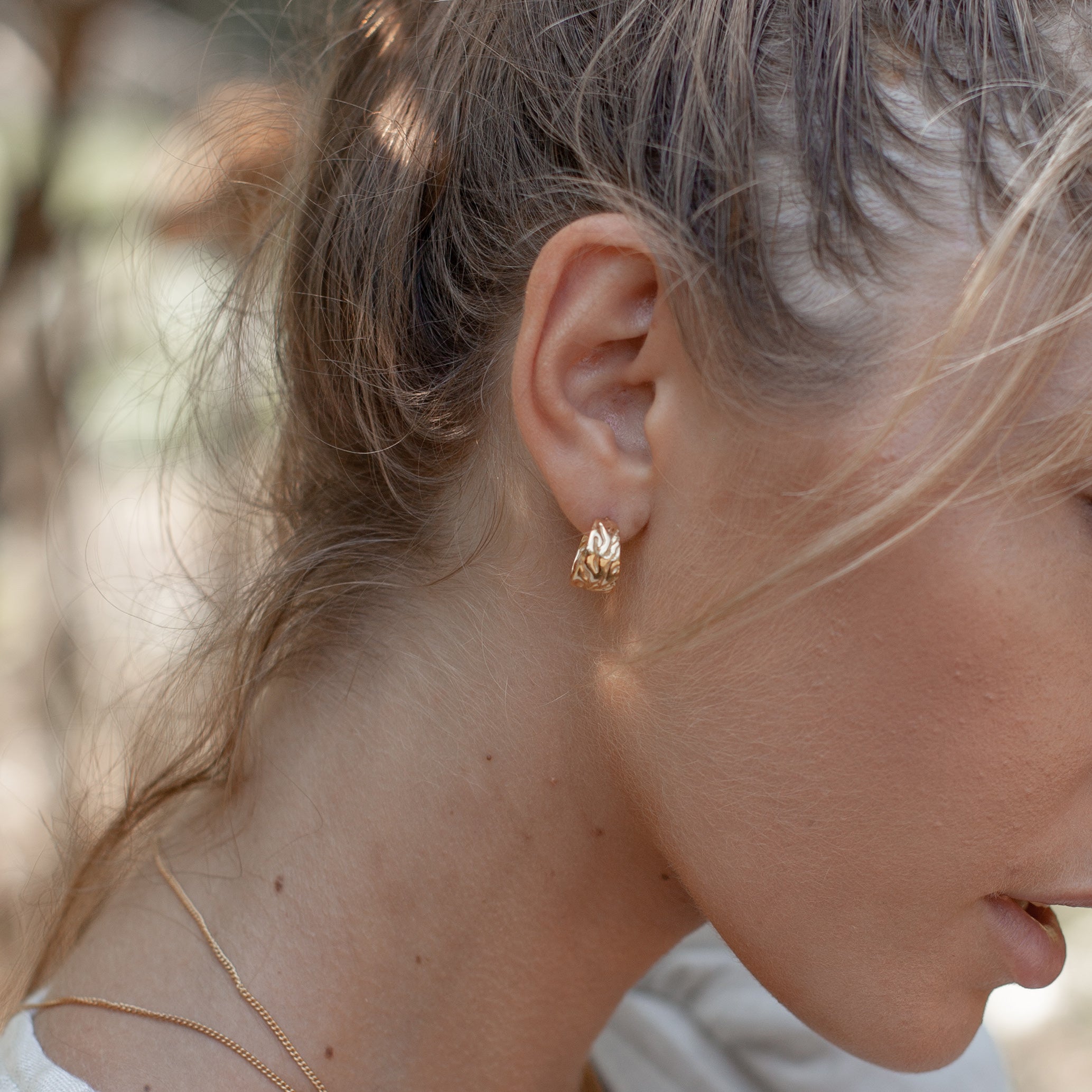 A person wearing a gold textured hoop earring, shown in profile.