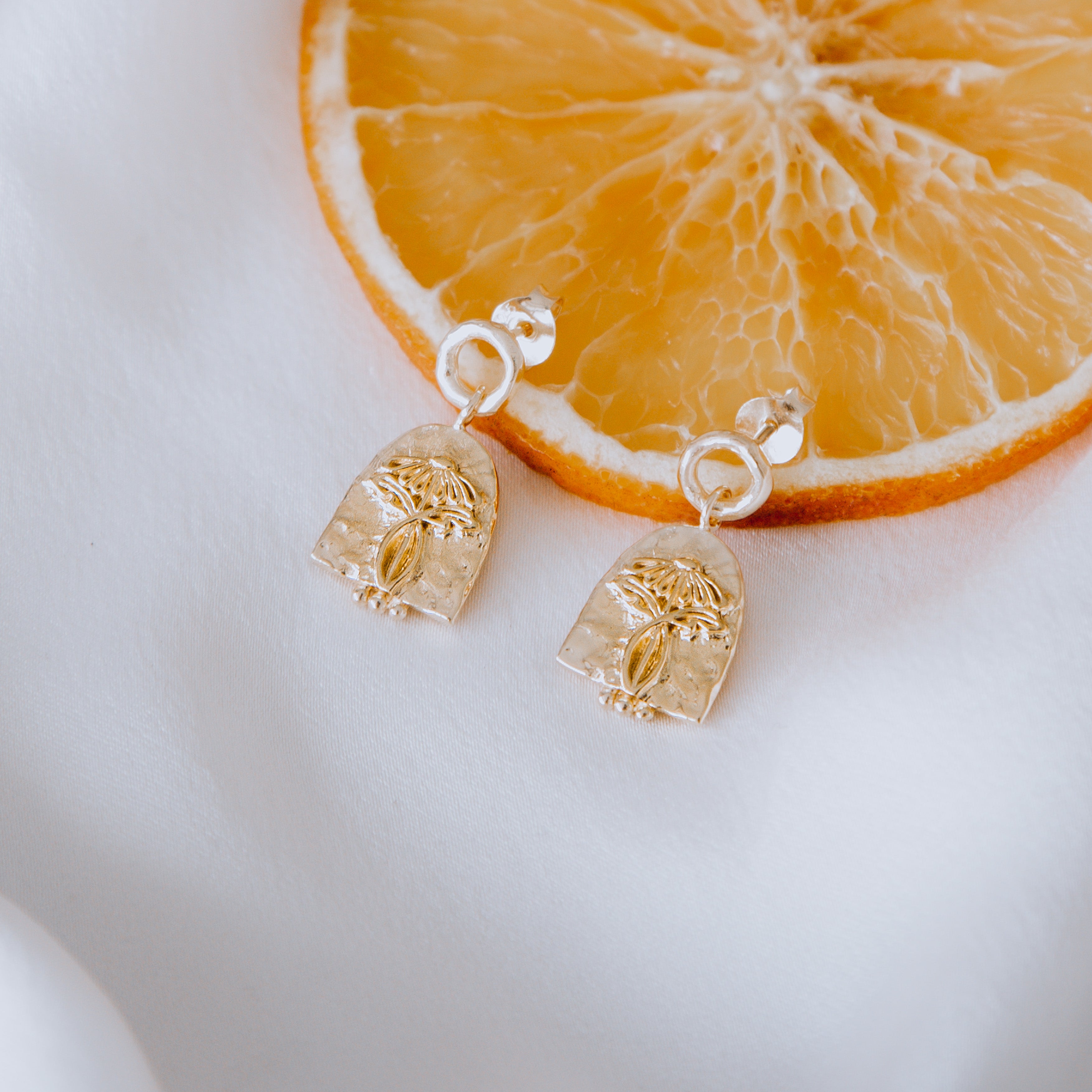 A close-up of a pair of golden earrings displayed agains a slice of orange