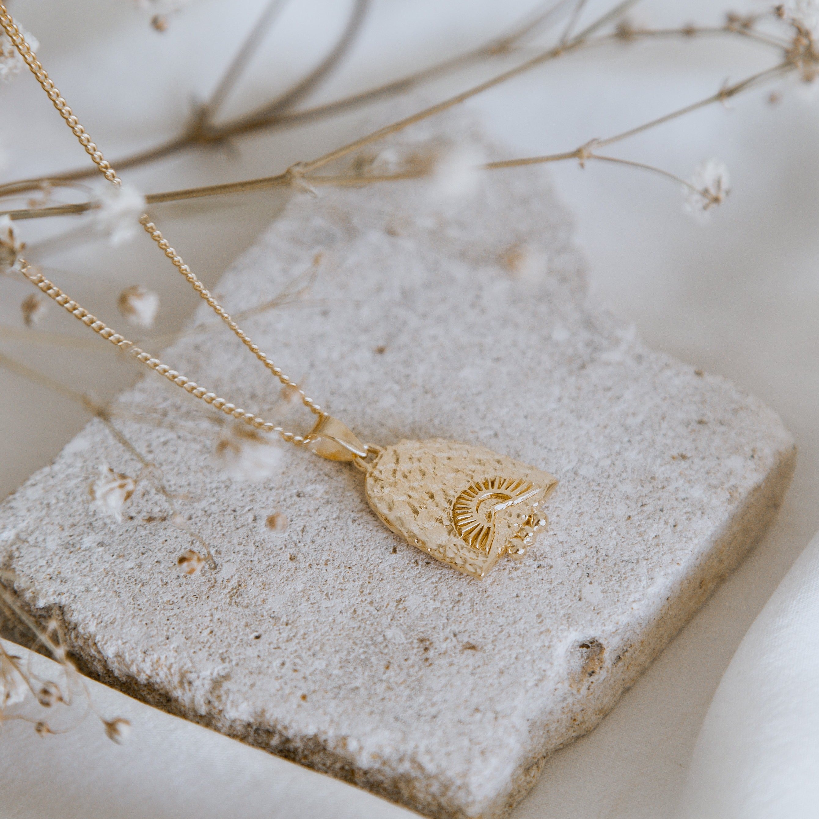 A close-up of a necklace displayed on a beige stone with delicate white flowers surrounding it.