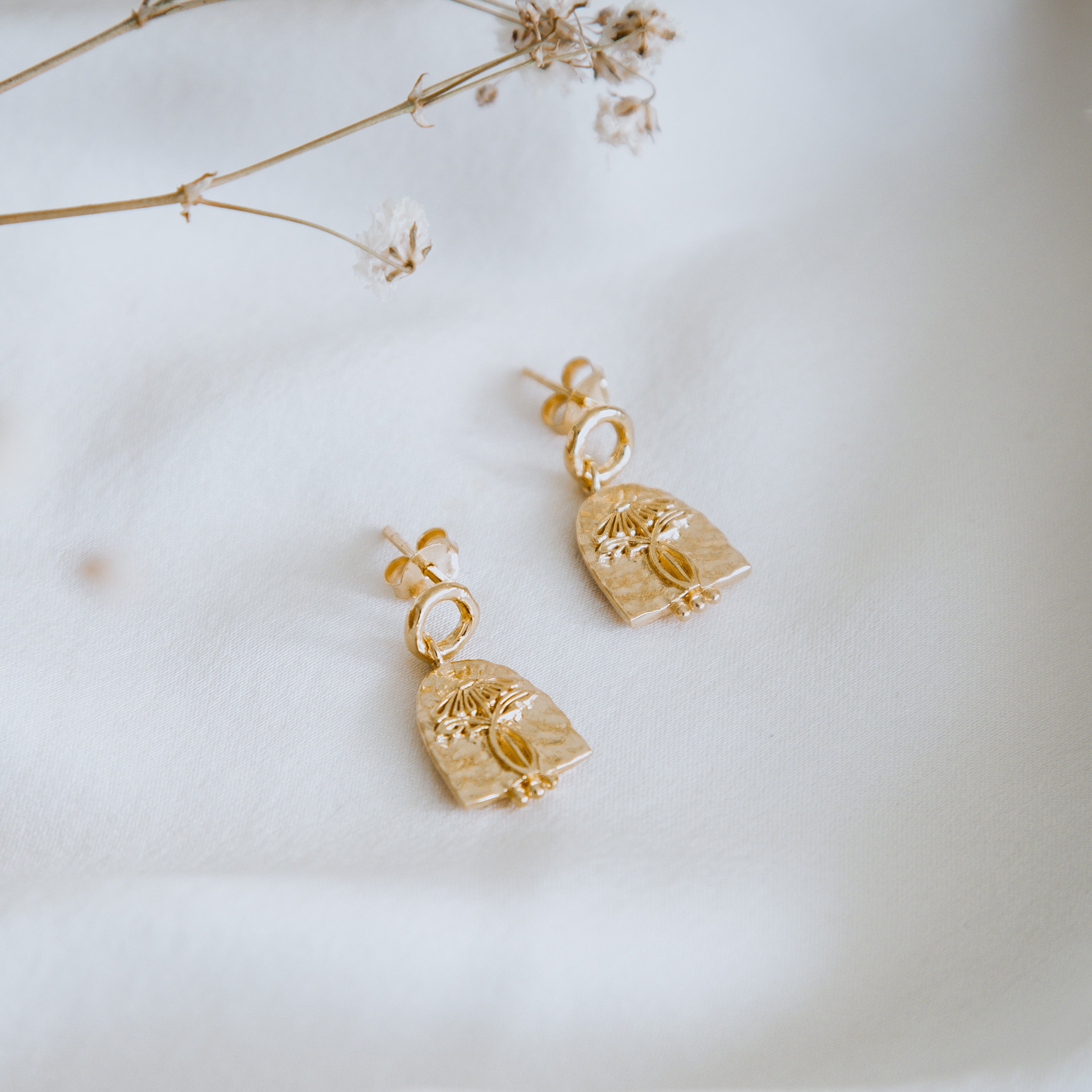 A close-up of golden earrings on a white backdrop with white flowers
