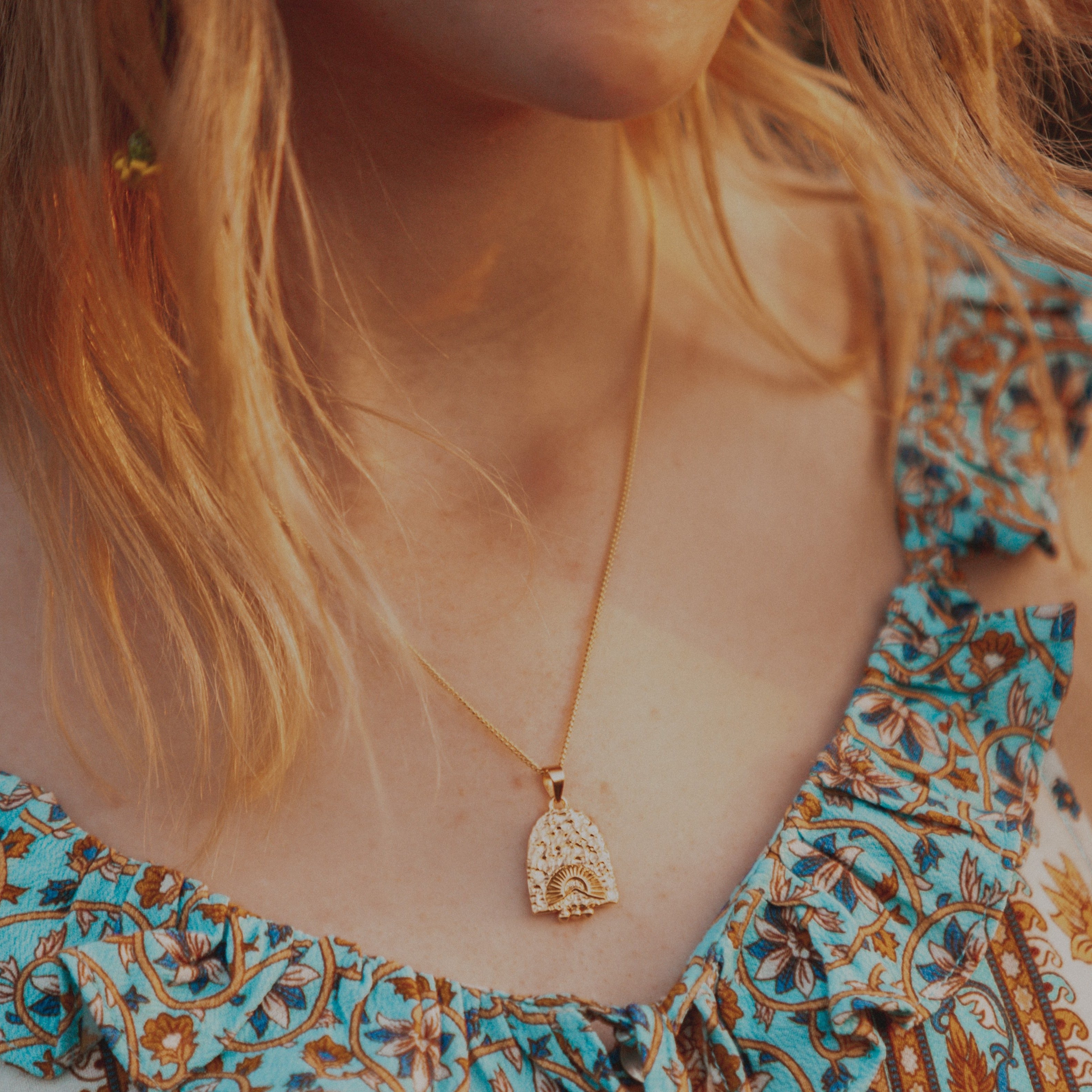 Close-up of a woman with red hair wearing a golden necklace.