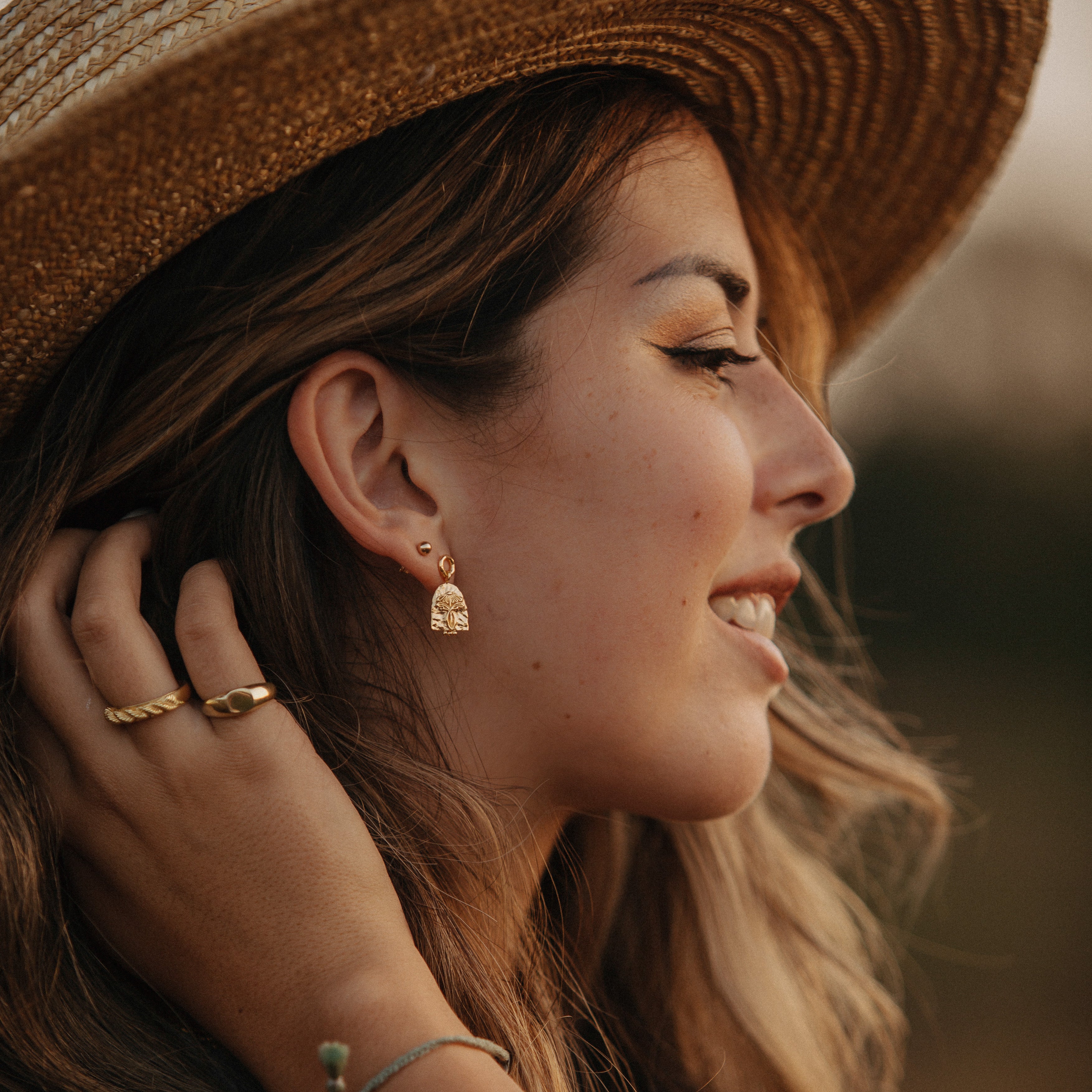 A woman with brown hair wearing a hat and jewellery