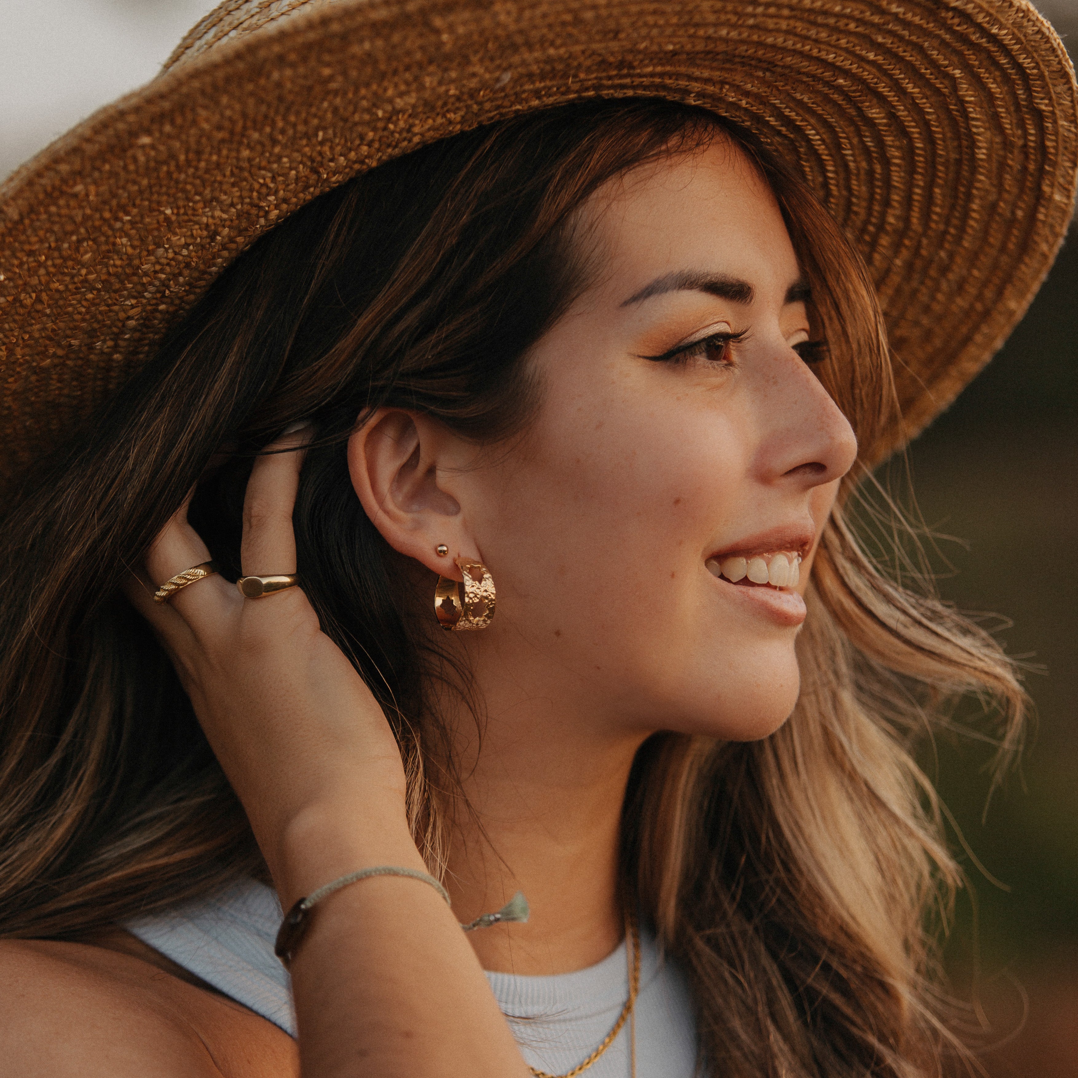 A woman with brown hair wearing a hat and jewellery
