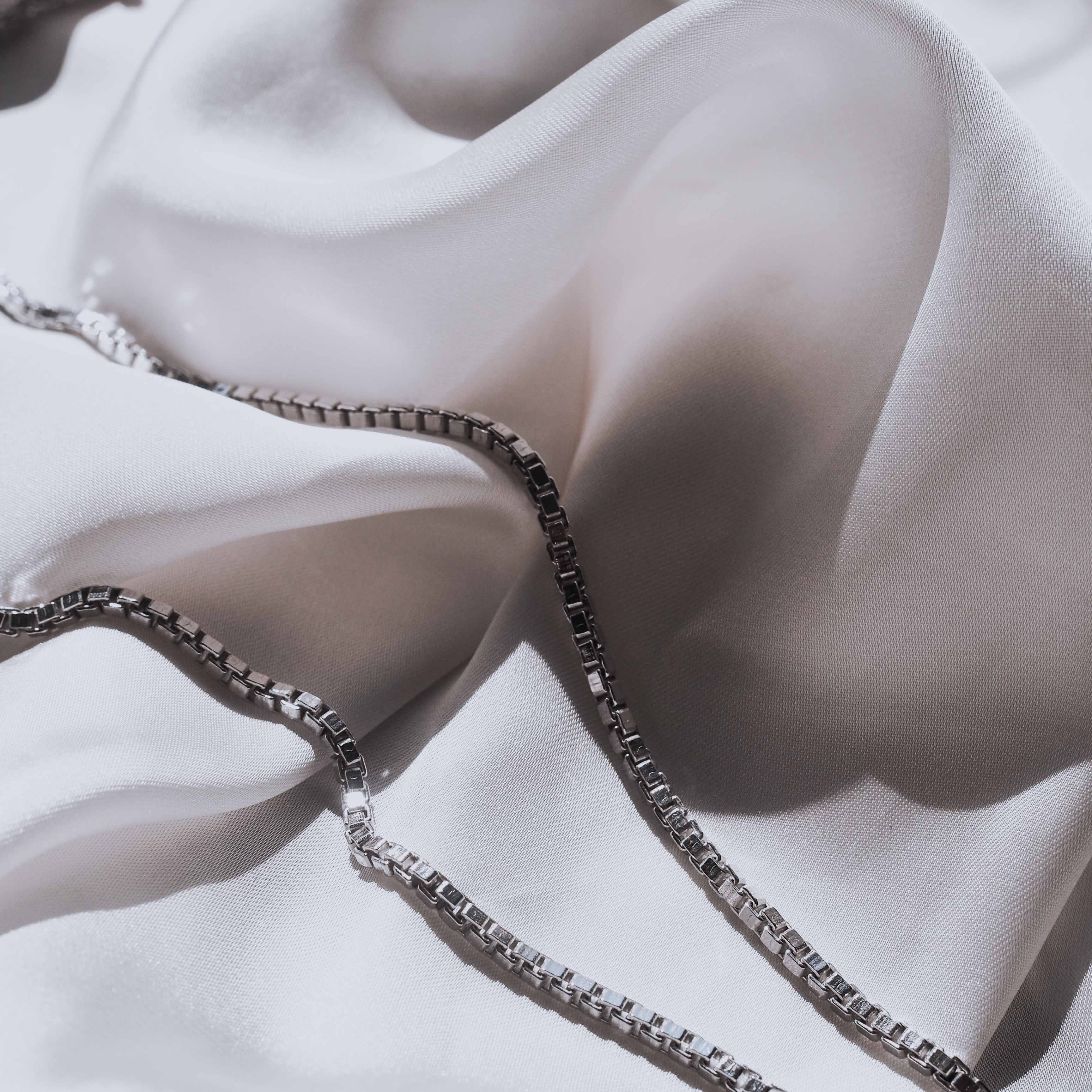 Close-up of a silver necklace and a satin fabric background