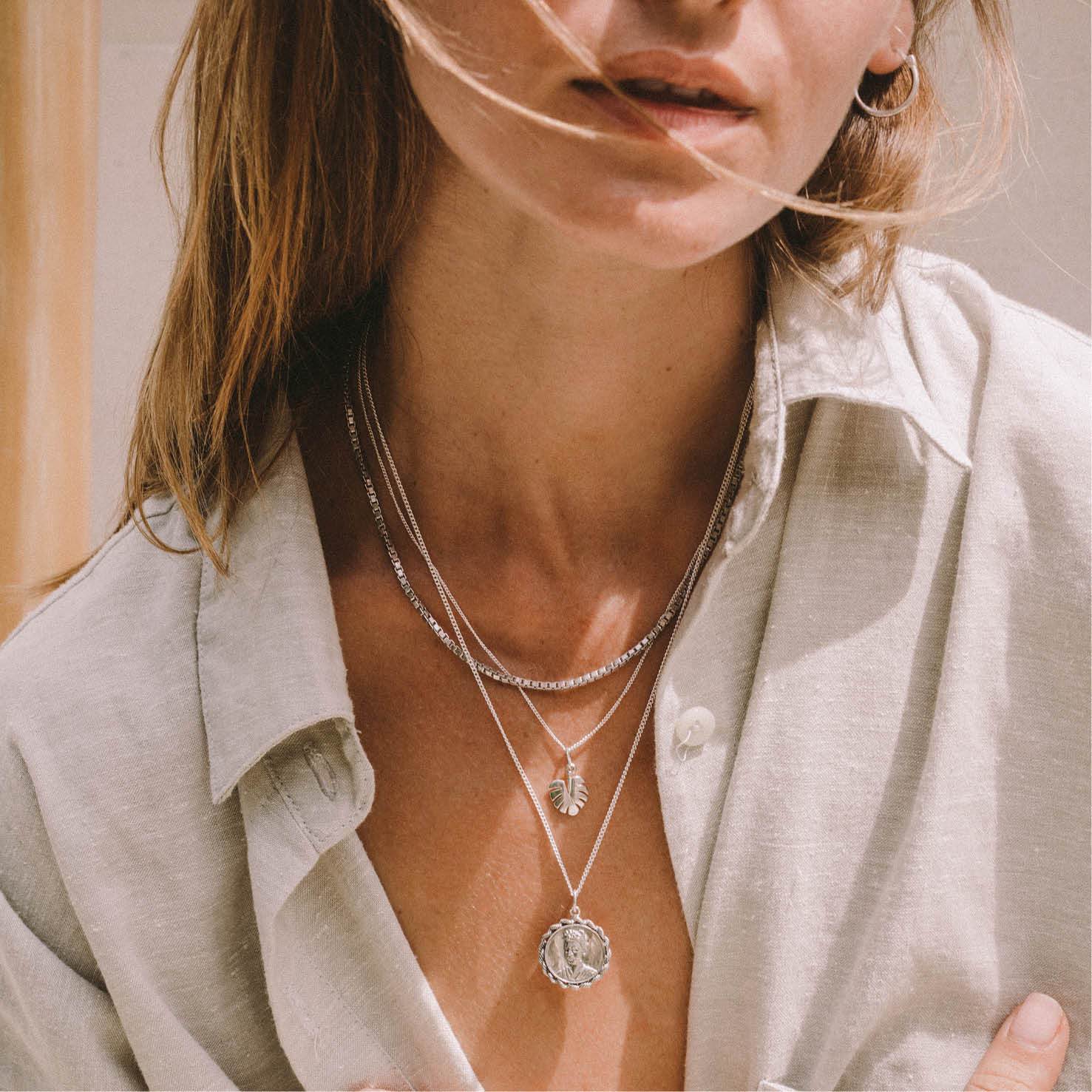 A close up of a woman wearing multiple silver necklaces and a grey blouse