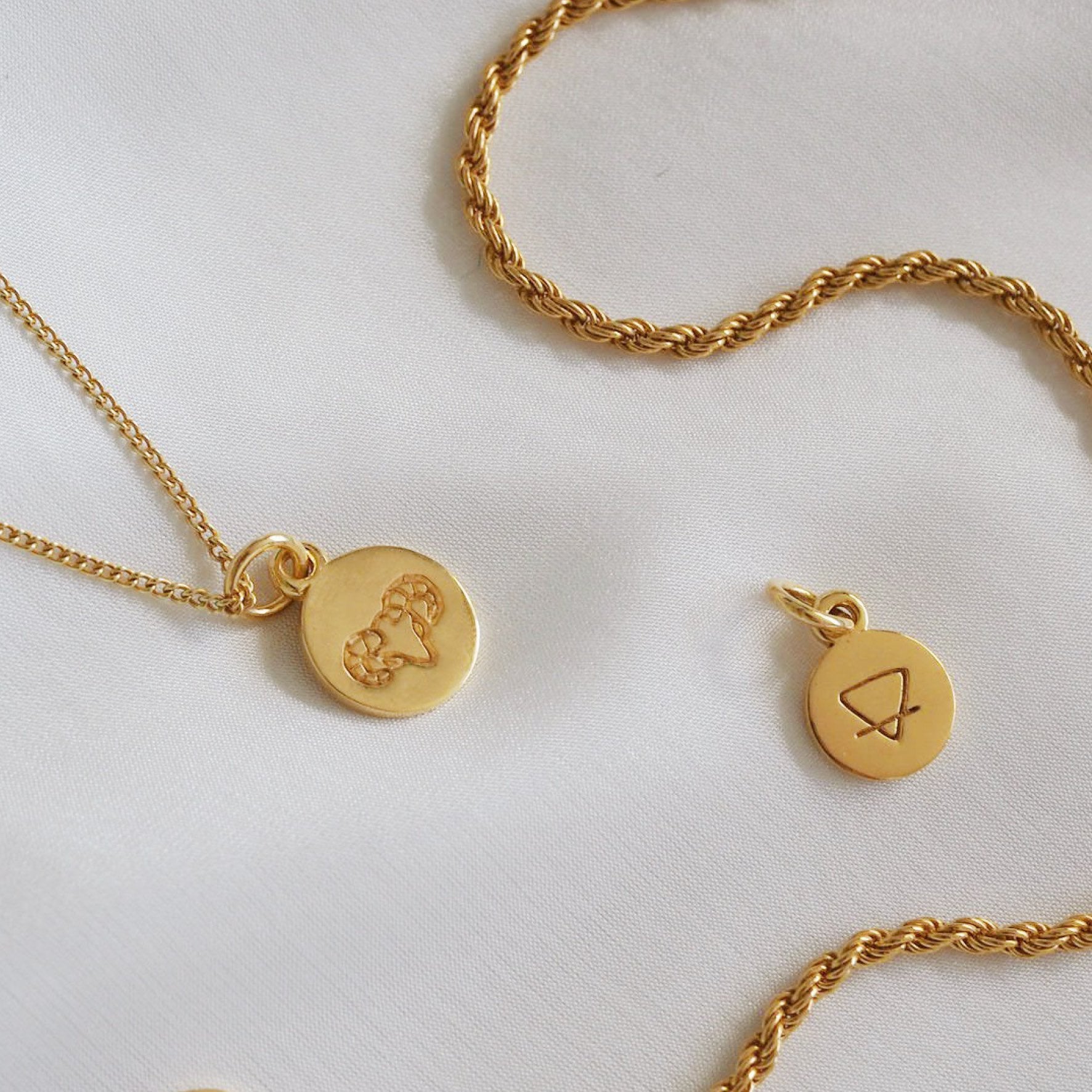 Two golden necklaces displayed on a white fabric backdrop.