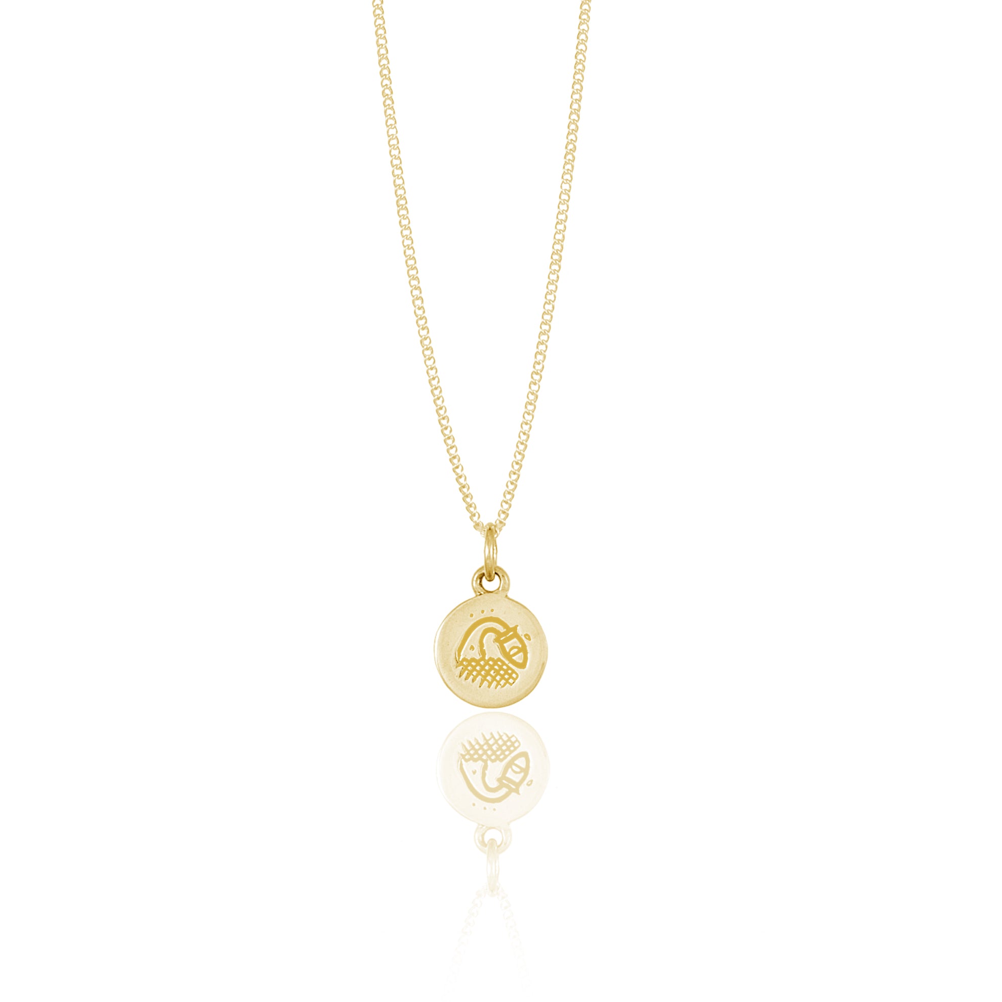 A small round gold pendant adorned with a minimalistic geometric design reflected on a white surface.