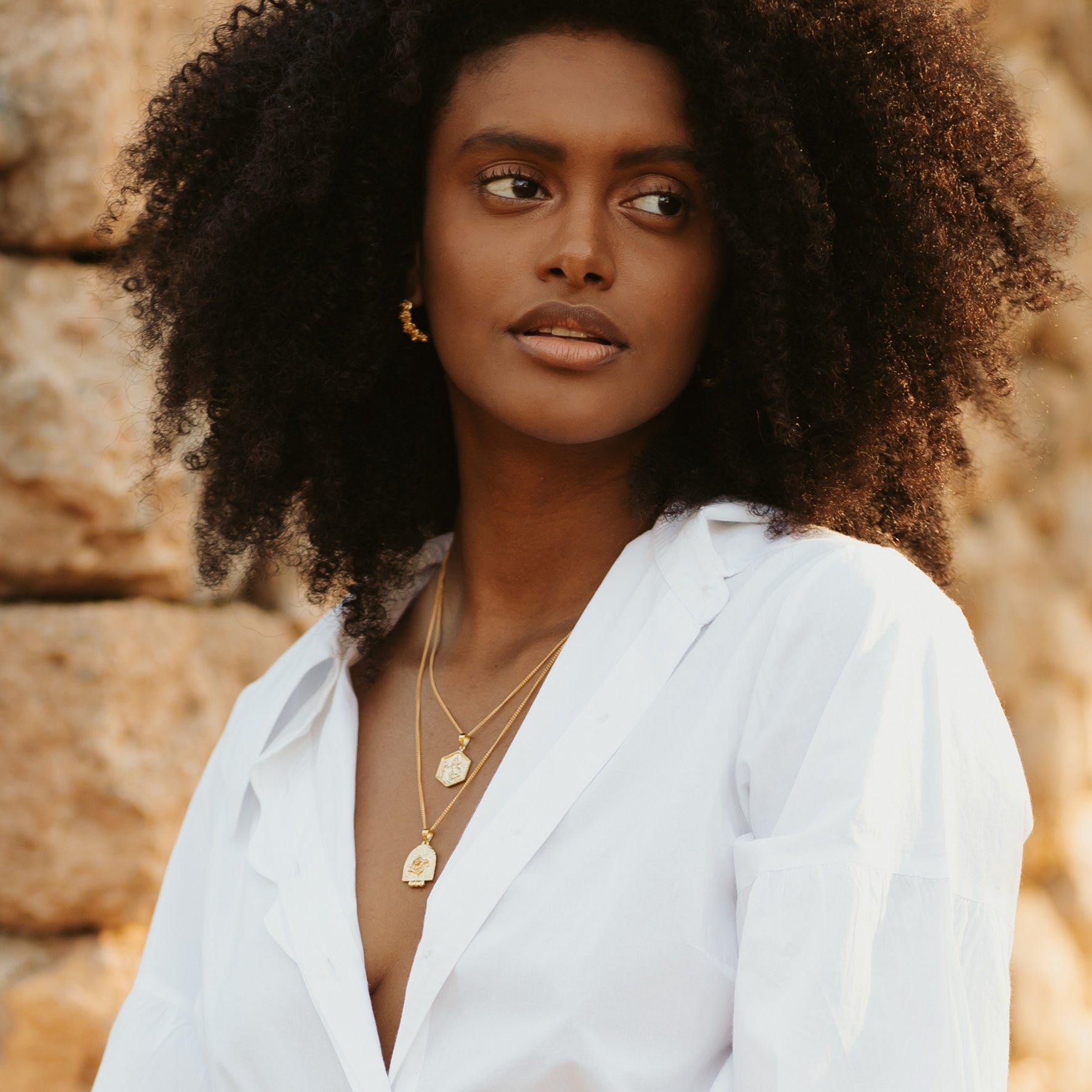 A woman with curly hair wearing golden jewellery and a white blouse