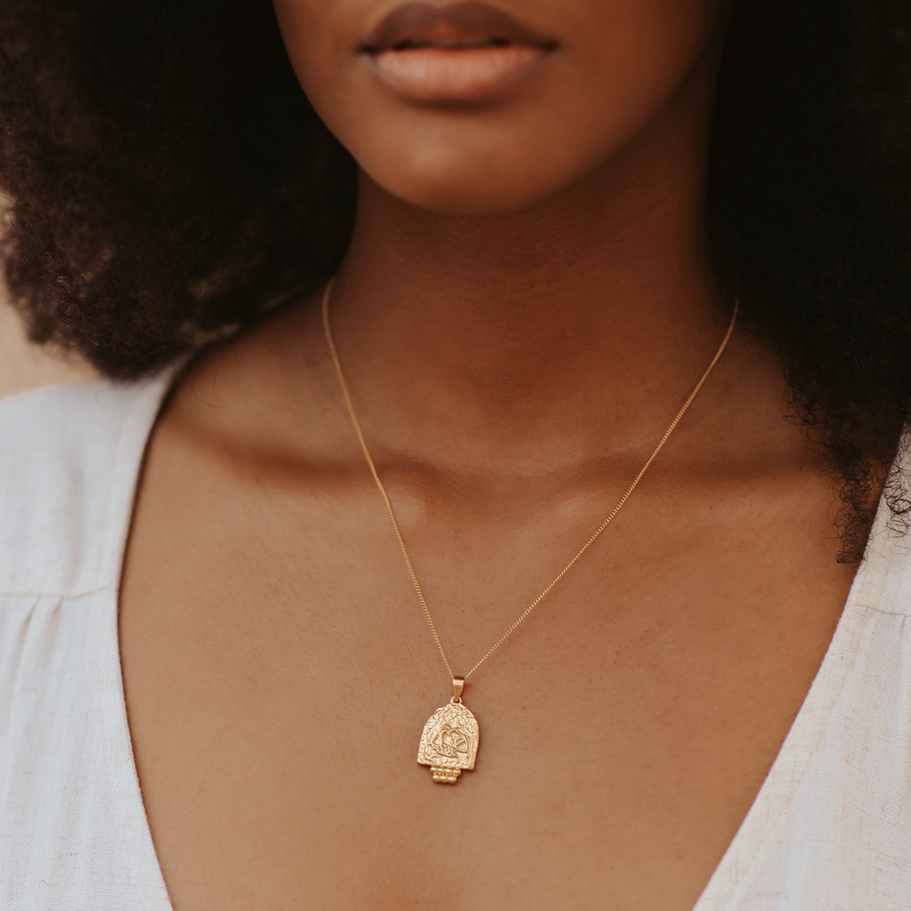 A woman with brown hair wearing a golden necklace and a white top
