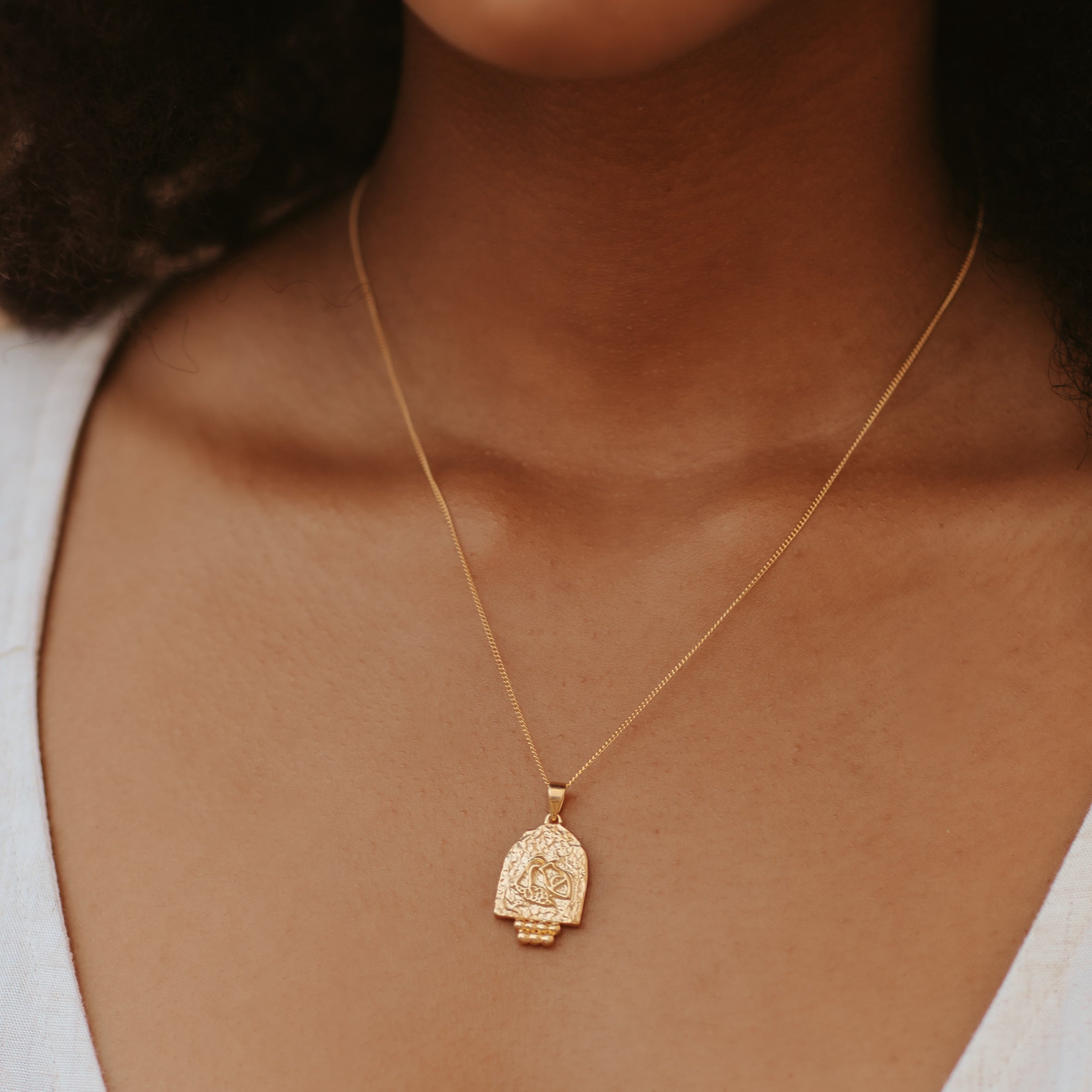 A woman with brown hair wearing a golden necklace and a white top
