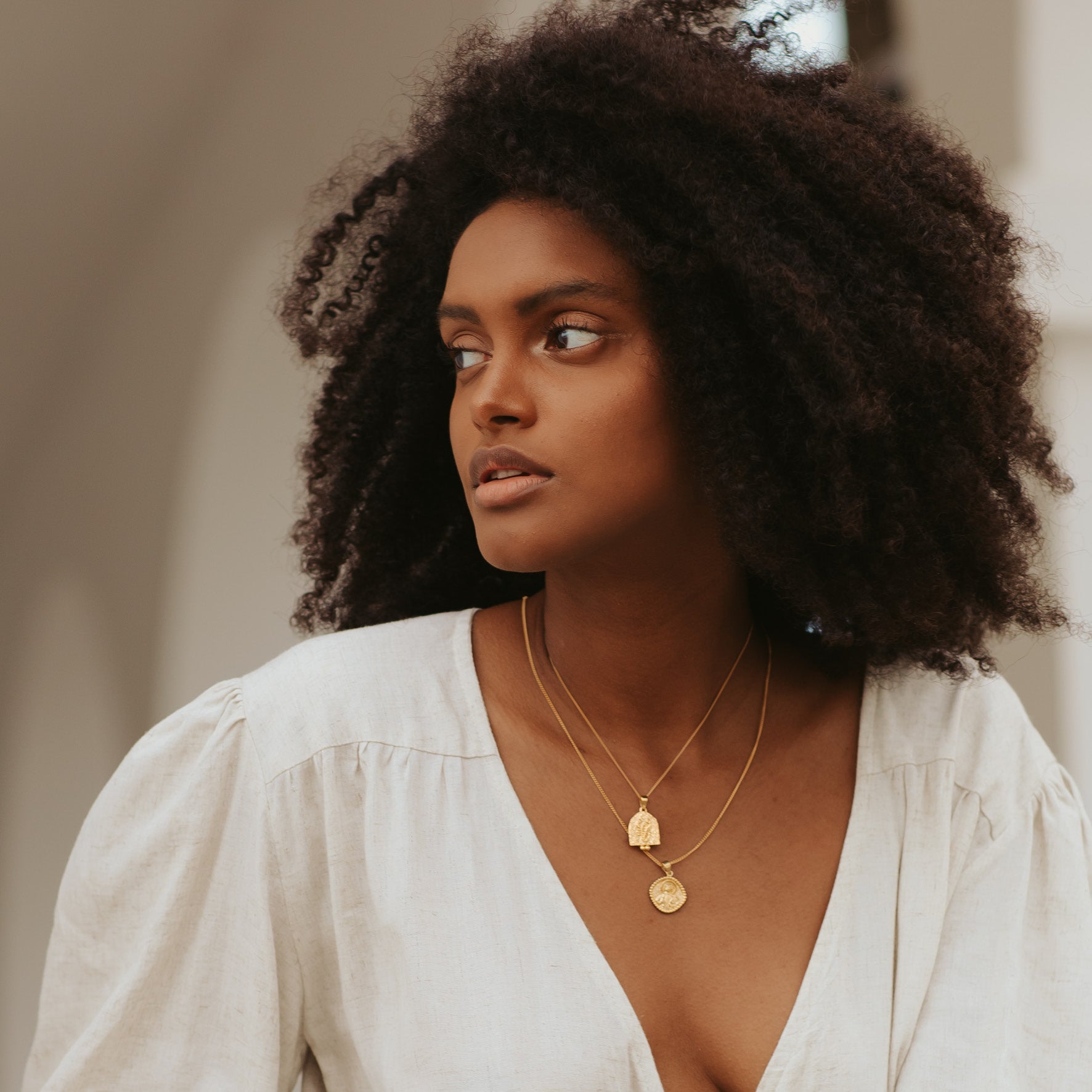 A woman with curly hair in a with top wearing two golden necklaces