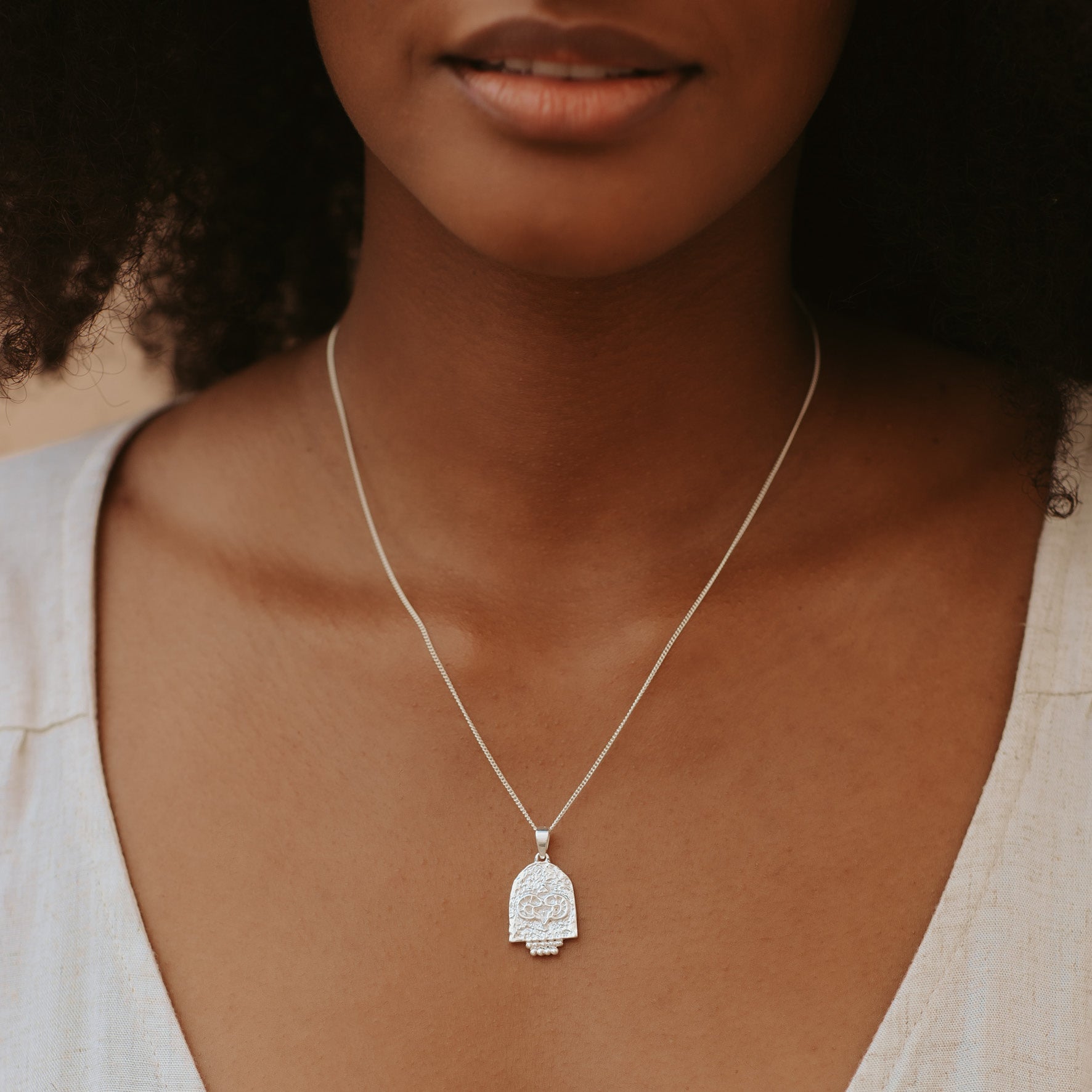 A woman with brown hair wearing a silver necklace and a white top