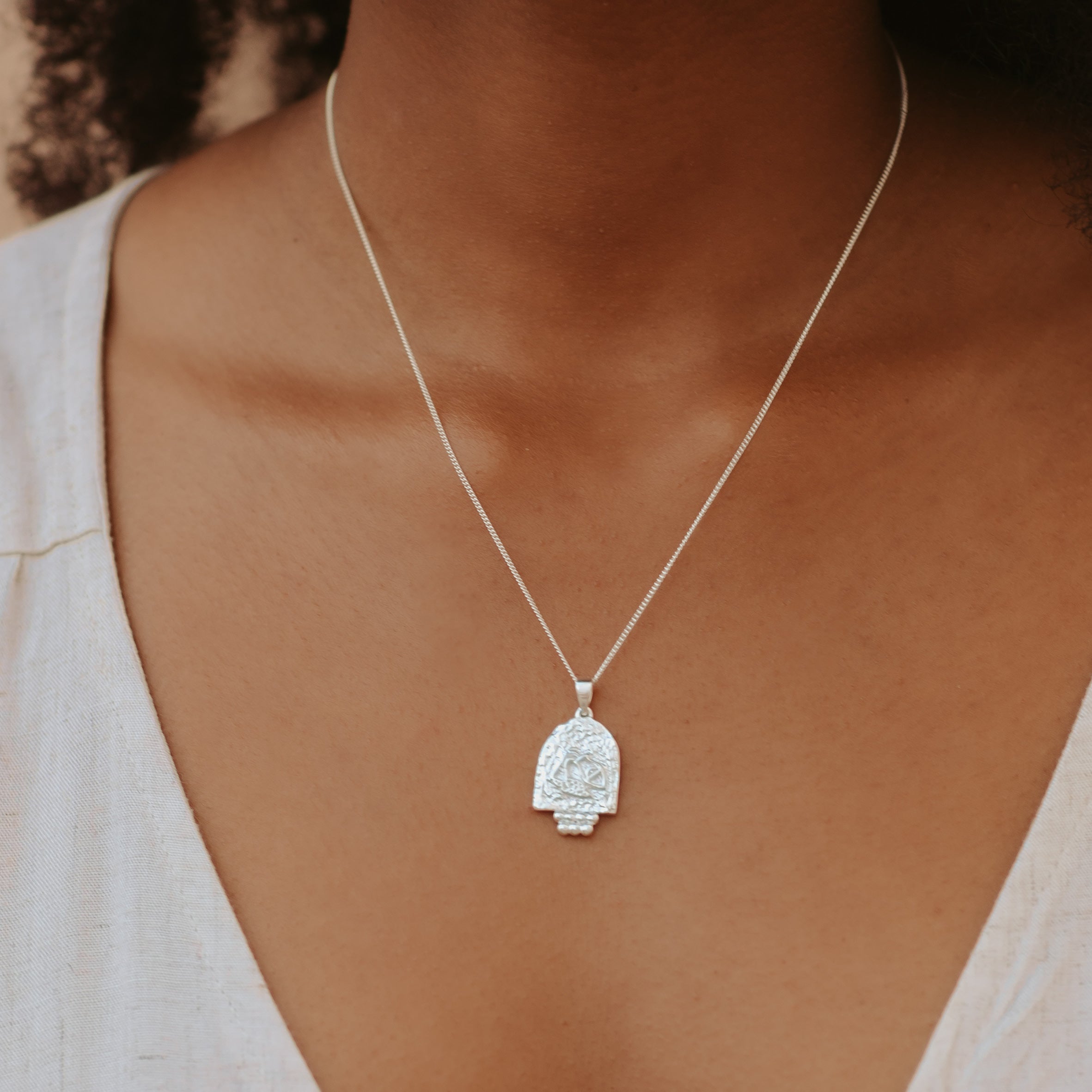 A close-up of a woman with brown hair wearing a silver necklace and a white top