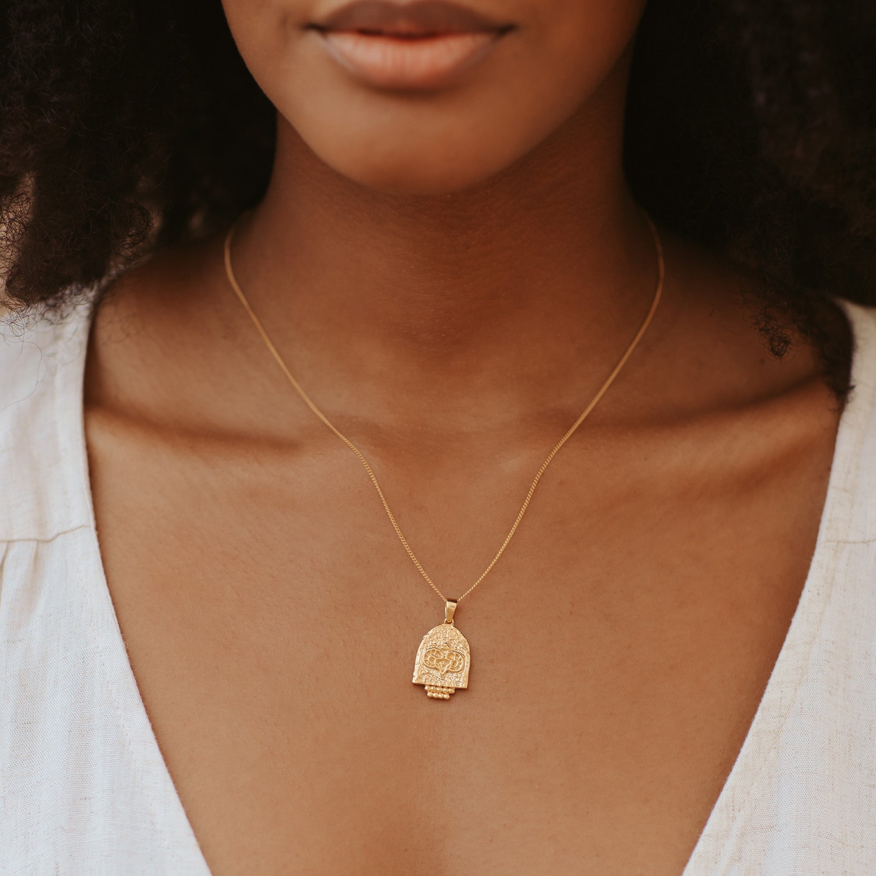 A woman with brown hair wearing a golden necklace and a white top