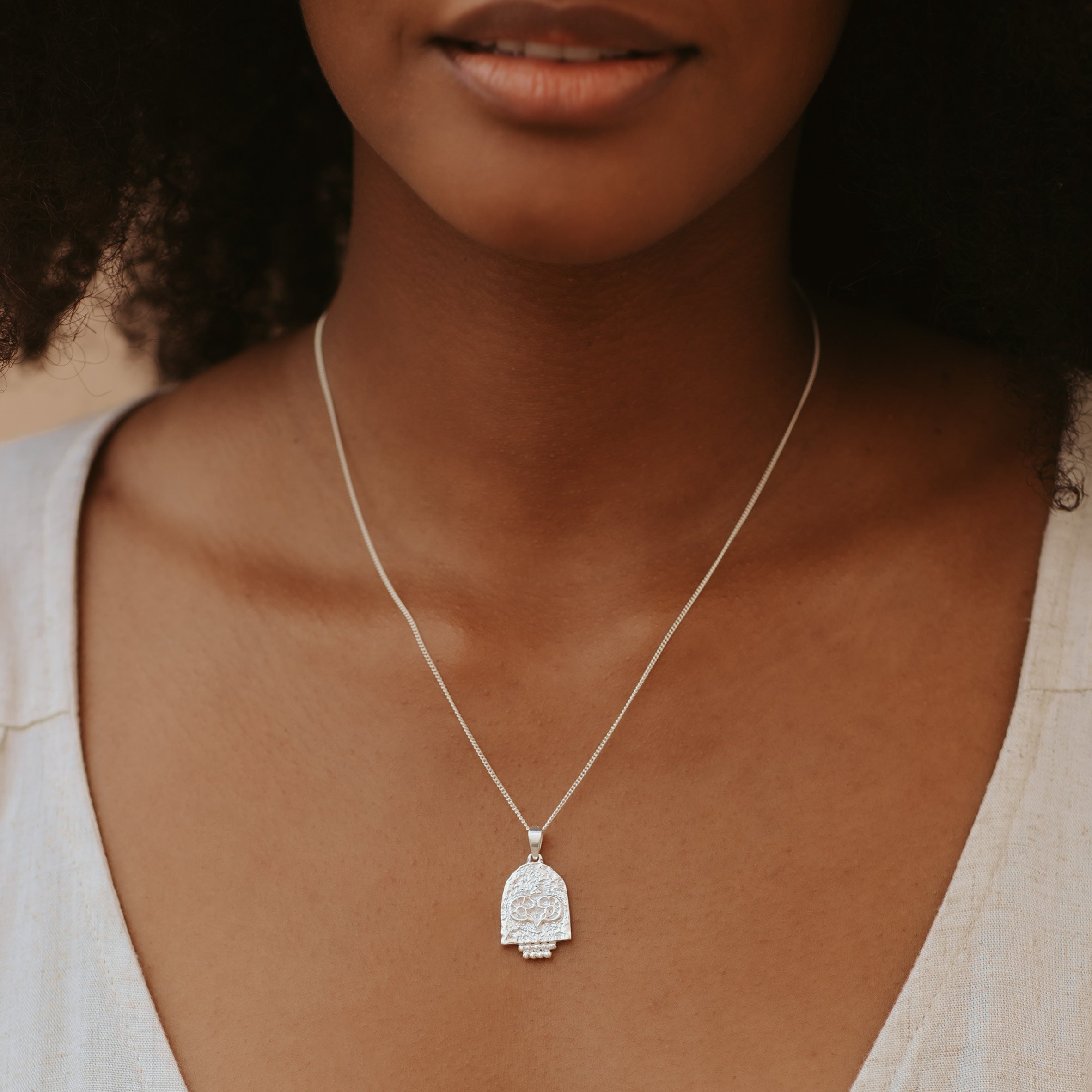 A woman with brown hair wearing a silver necklace and a white top