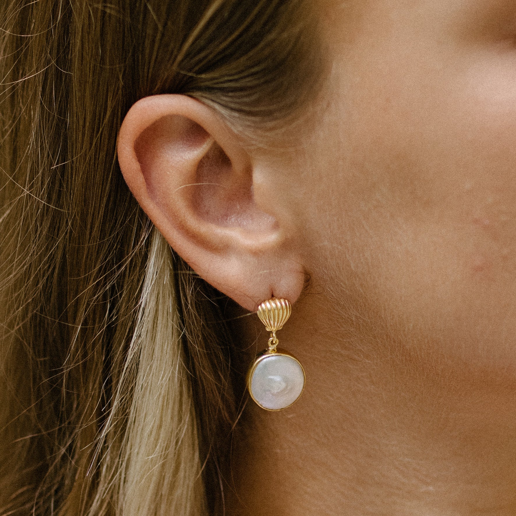 Close-up of a person's ear wearing a gold drop earring with a large white pearl pendant.