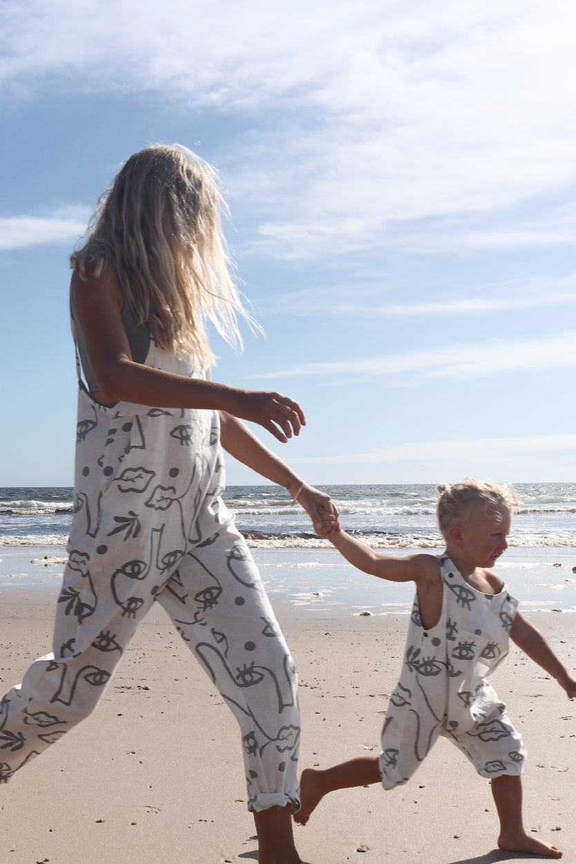 A toddler together with a woman walking on the beach in a overall