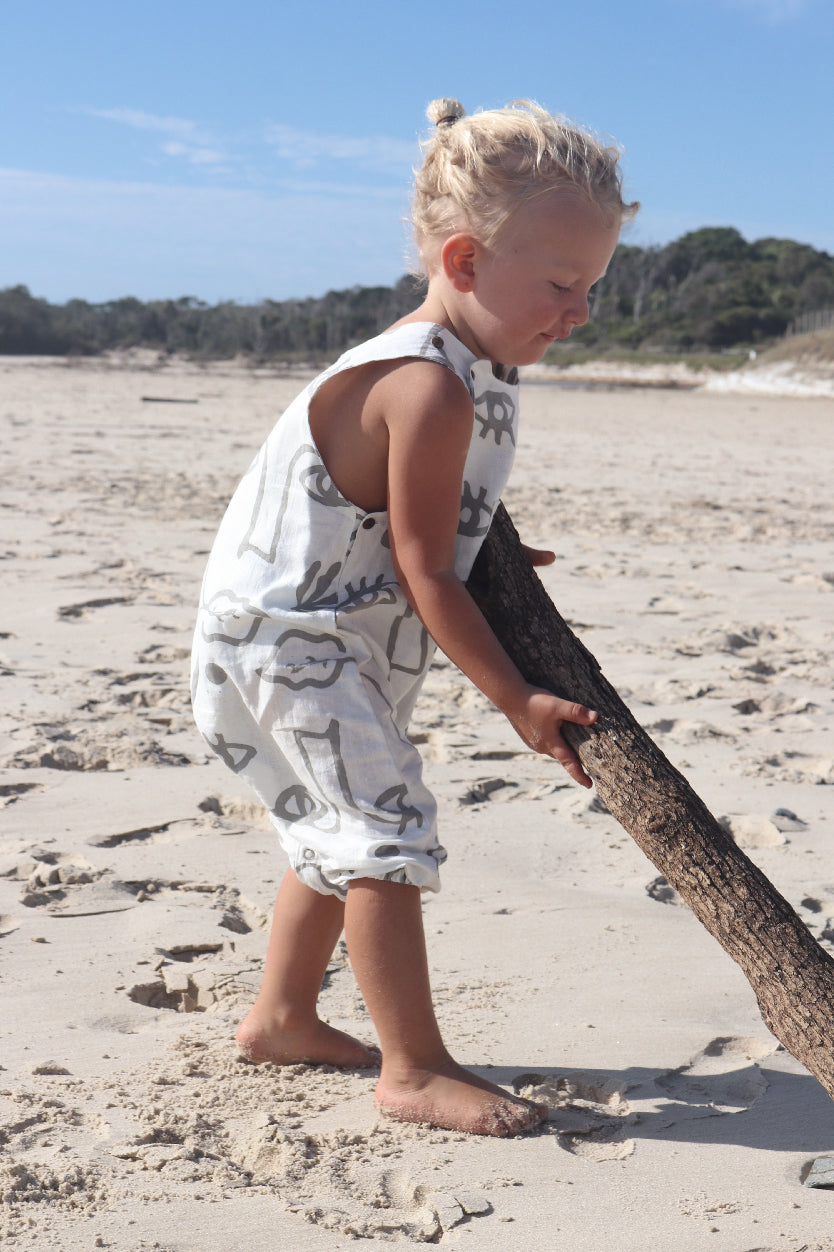 A toddler playing around on the beach in an overall