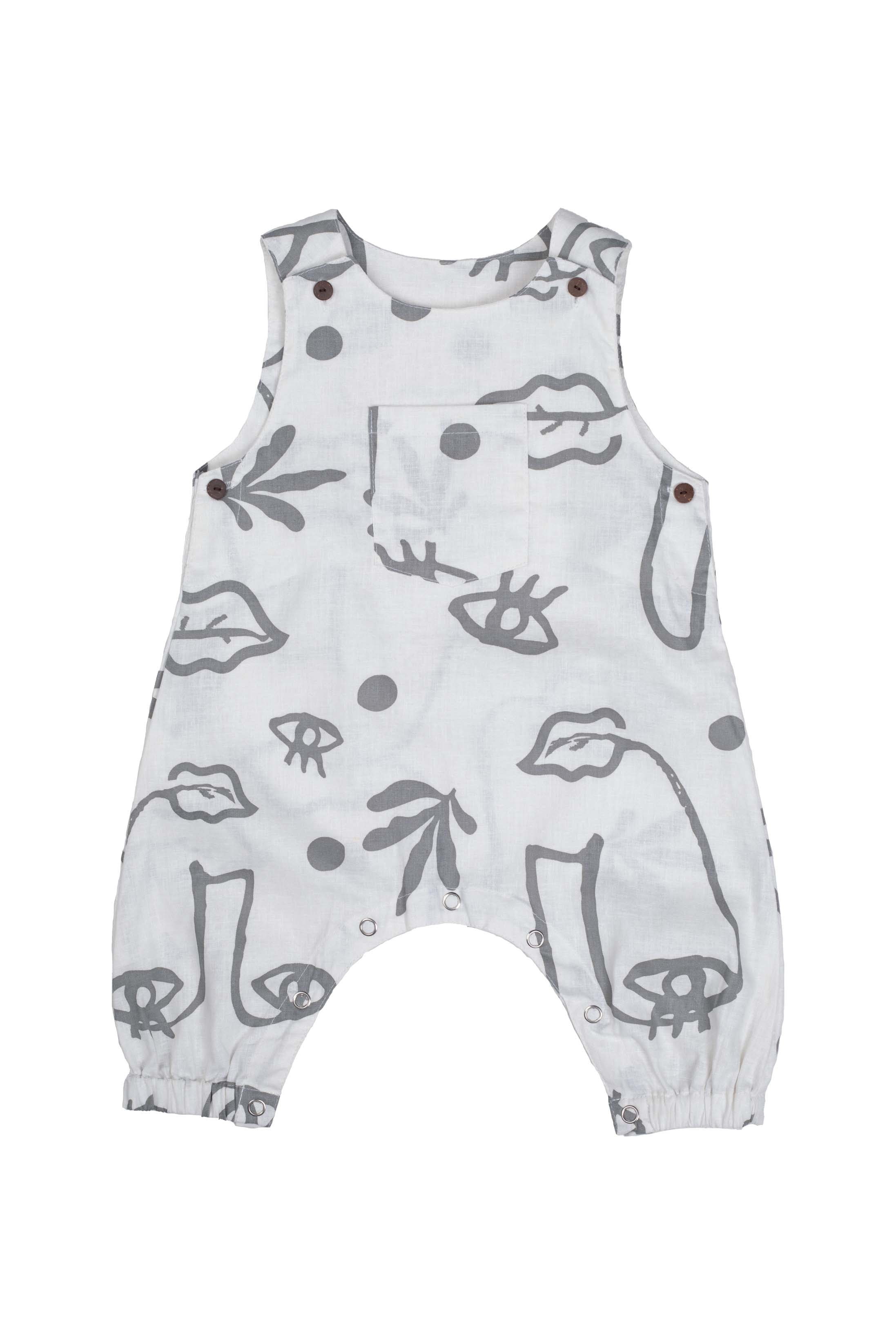 A grey romper with grey abstract face designs and snap buttons along the legs and shoulders is laid flat on a white blackground