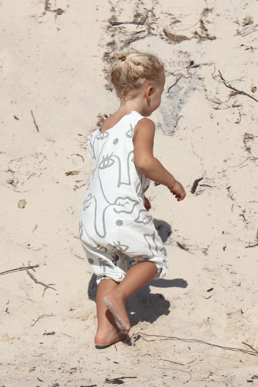 A toddler walking on the beach in a white overall