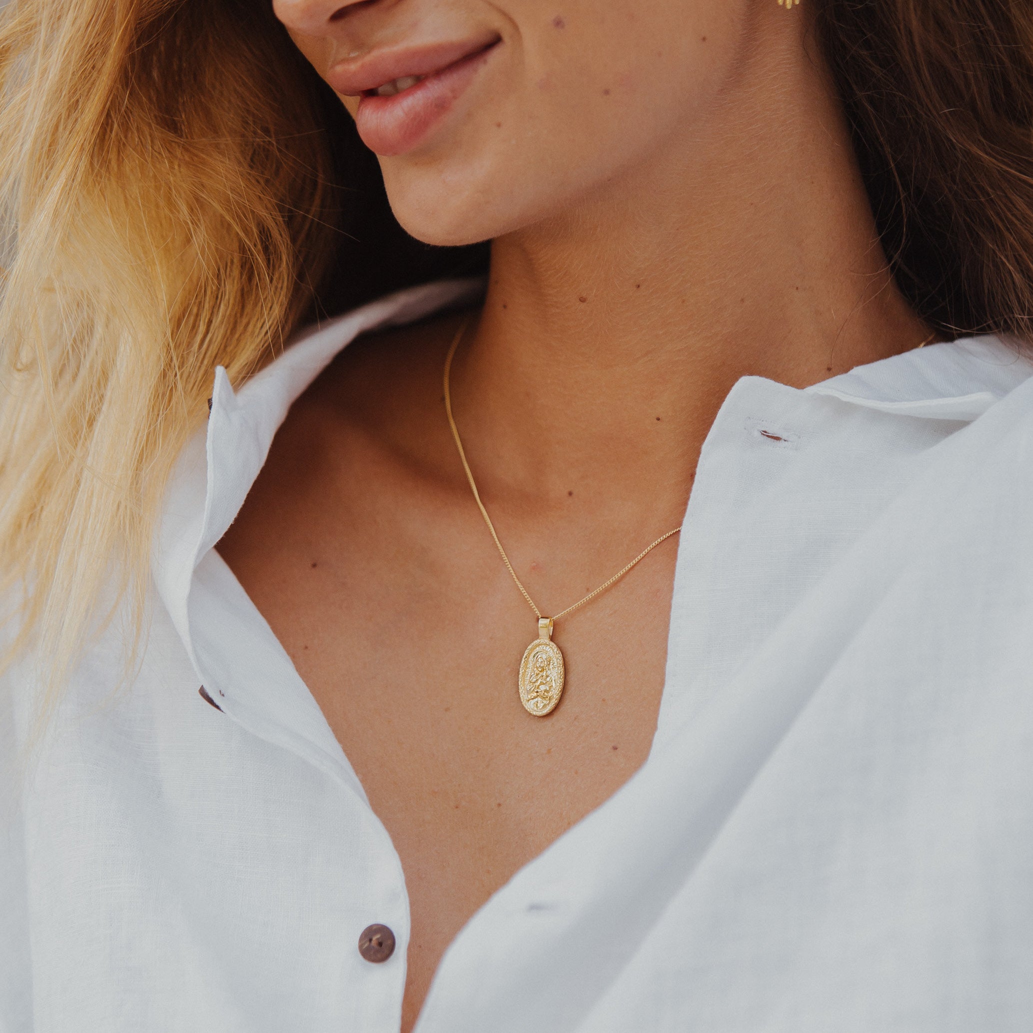 A smiling woman with brunette hair wearing gold necklace and a white blouse.